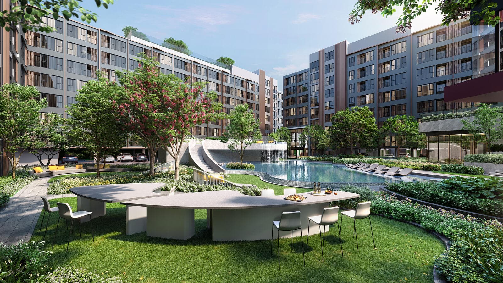 Landscaped garden courtyard at Atmoz Flow Minburi with a large communal table on the lawn, a water slide and swimming pool beyond, framed by the residential buildings (computer-generated render)