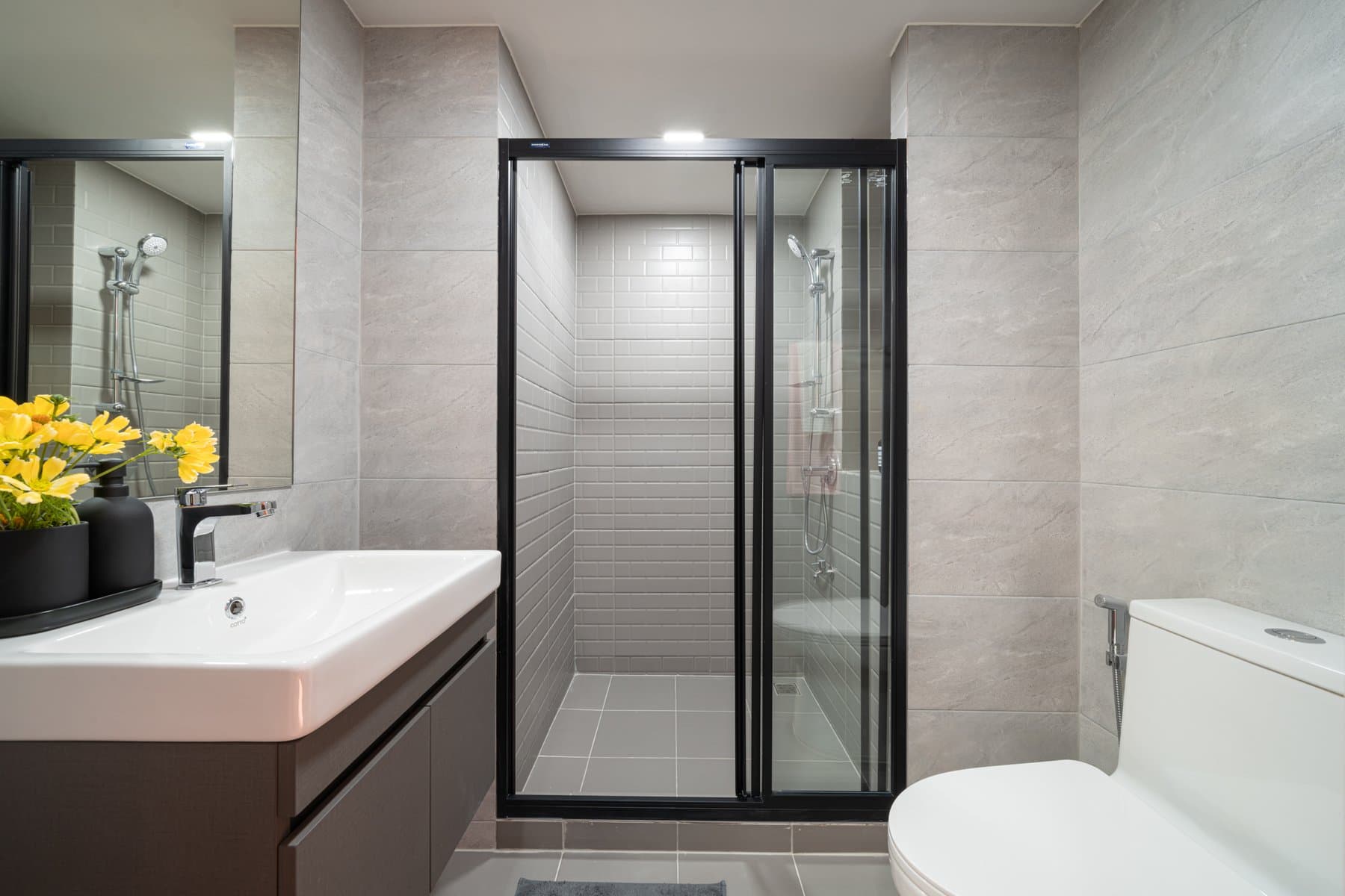 Bathroom in a furnished show unit at Atmoz Flow Minburi, with a wall-hung basin on a dark vanity, a mirrored cabinet and a framed glass shower enclosure