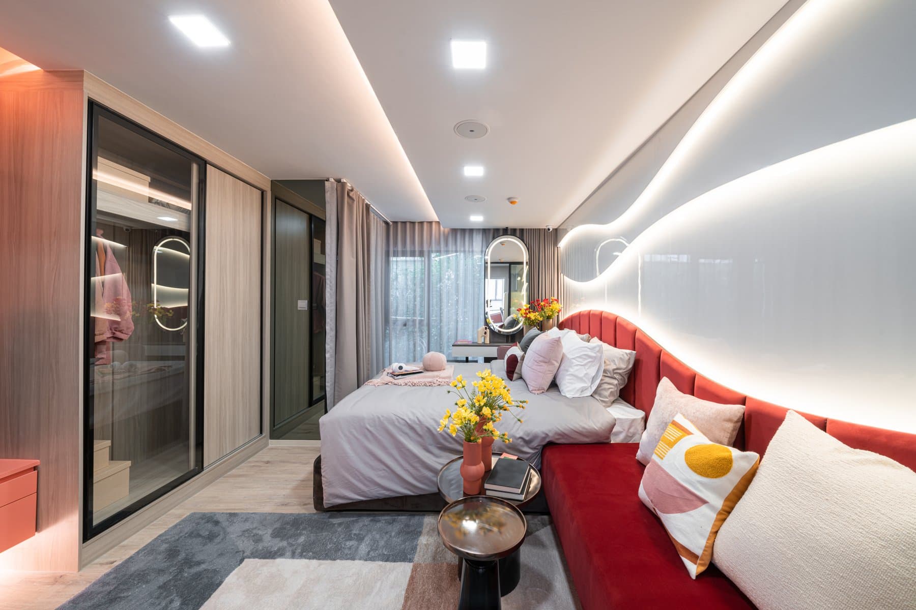 Living area of a furnished show unit at Atmoz Flow Minburi, with a red sofa, a low round table and a ribbon of cove lighting sweeping across the ceiling