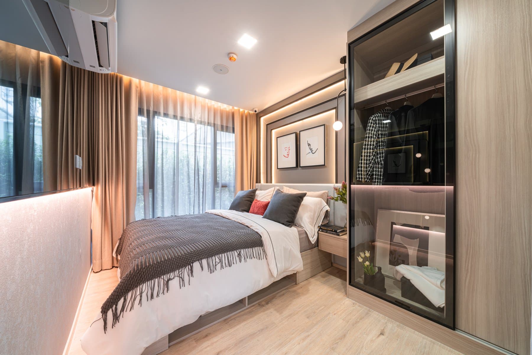 Bedroom of a larger furnished show unit at Atmoz Flow Minburi, with fluted timber panelling, layered bedding and sheer curtains across the window wall