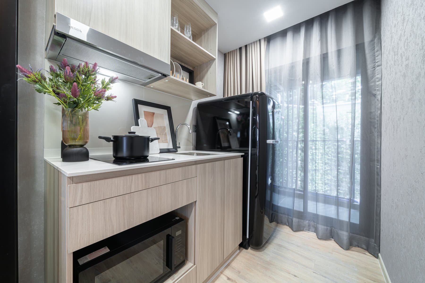 Kitchen counter in a larger furnished show unit at Atmoz Flow Minburi, with an extractor hood, a hob and a coffee machine against a sheer-curtained window