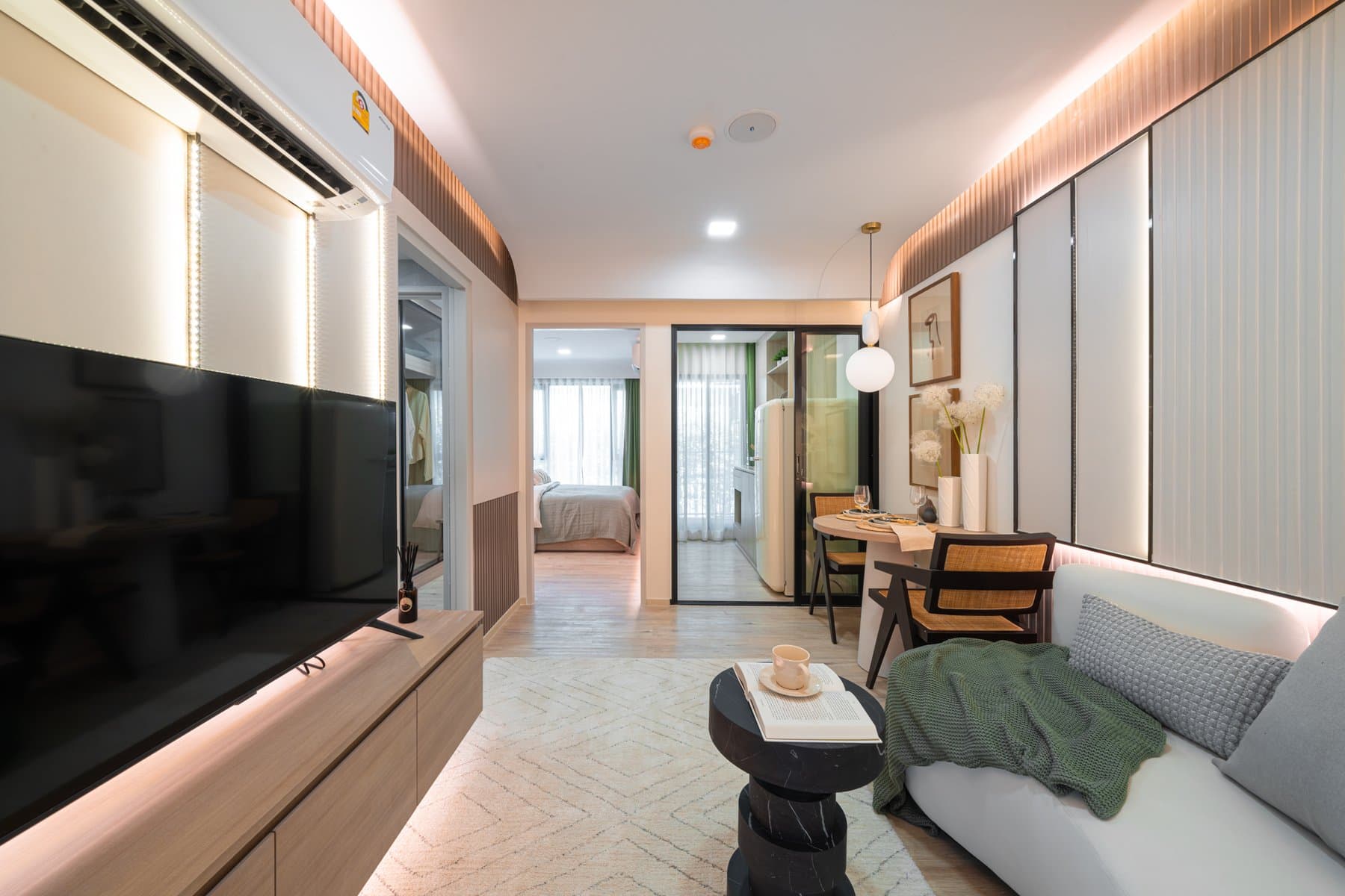 Full length of a larger furnished show unit at Atmoz Flow Minburi, from the television wall through to the dining table and the daylit window