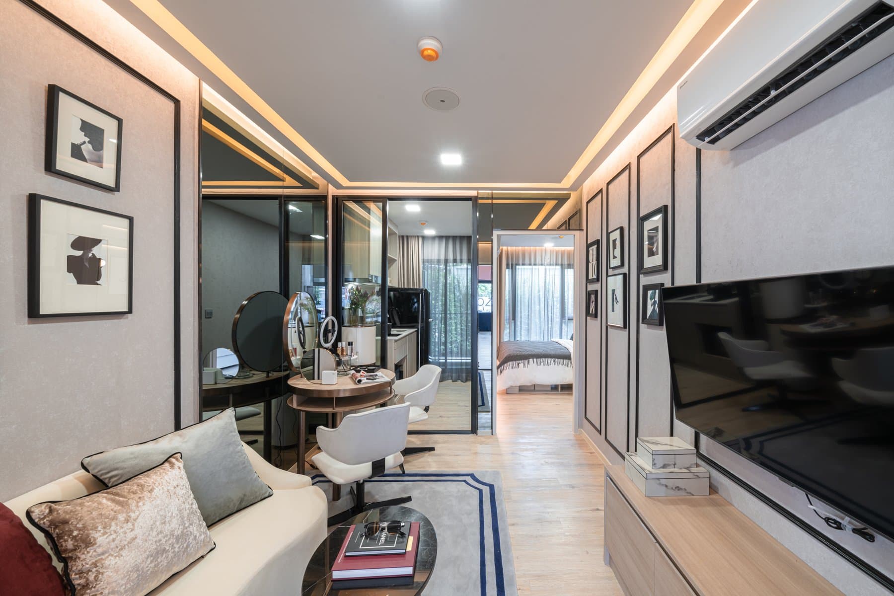 Living area of a larger furnished show unit at Atmoz Flow Minburi, with a cream sofa, a gallery wall of framed prints and a dressing corner in the background