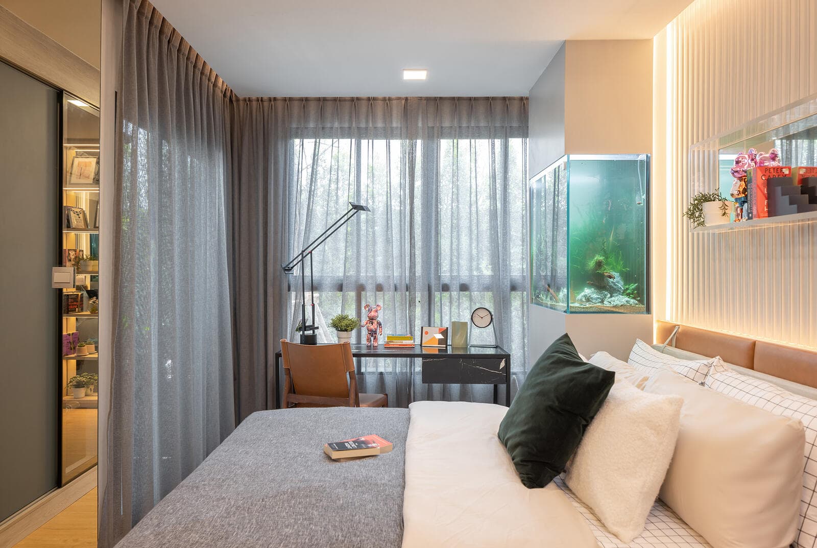 Sleeping area of the Atmoz Kanaal Rangsit show unit with a full-height sheer-curtained window, built-in desk and lamp beside the bed