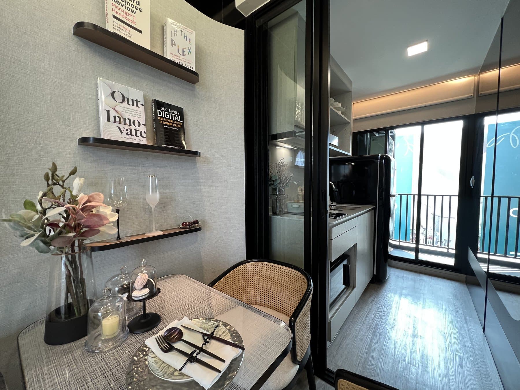 Dining nook in a furnished show unit at Atmoz Oasis Onnut, with a laid table, floating shelves and the balcony door beyond