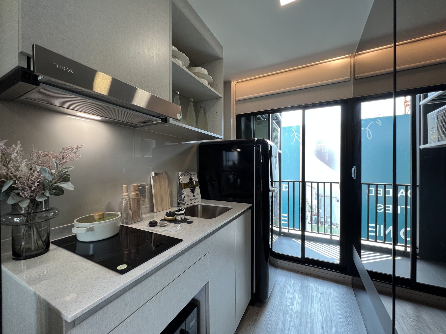 Kitchen run in a furnished show unit at Atmoz Oasis Onnut, with a black hob, an extractor and a glazed door opening to the balcony