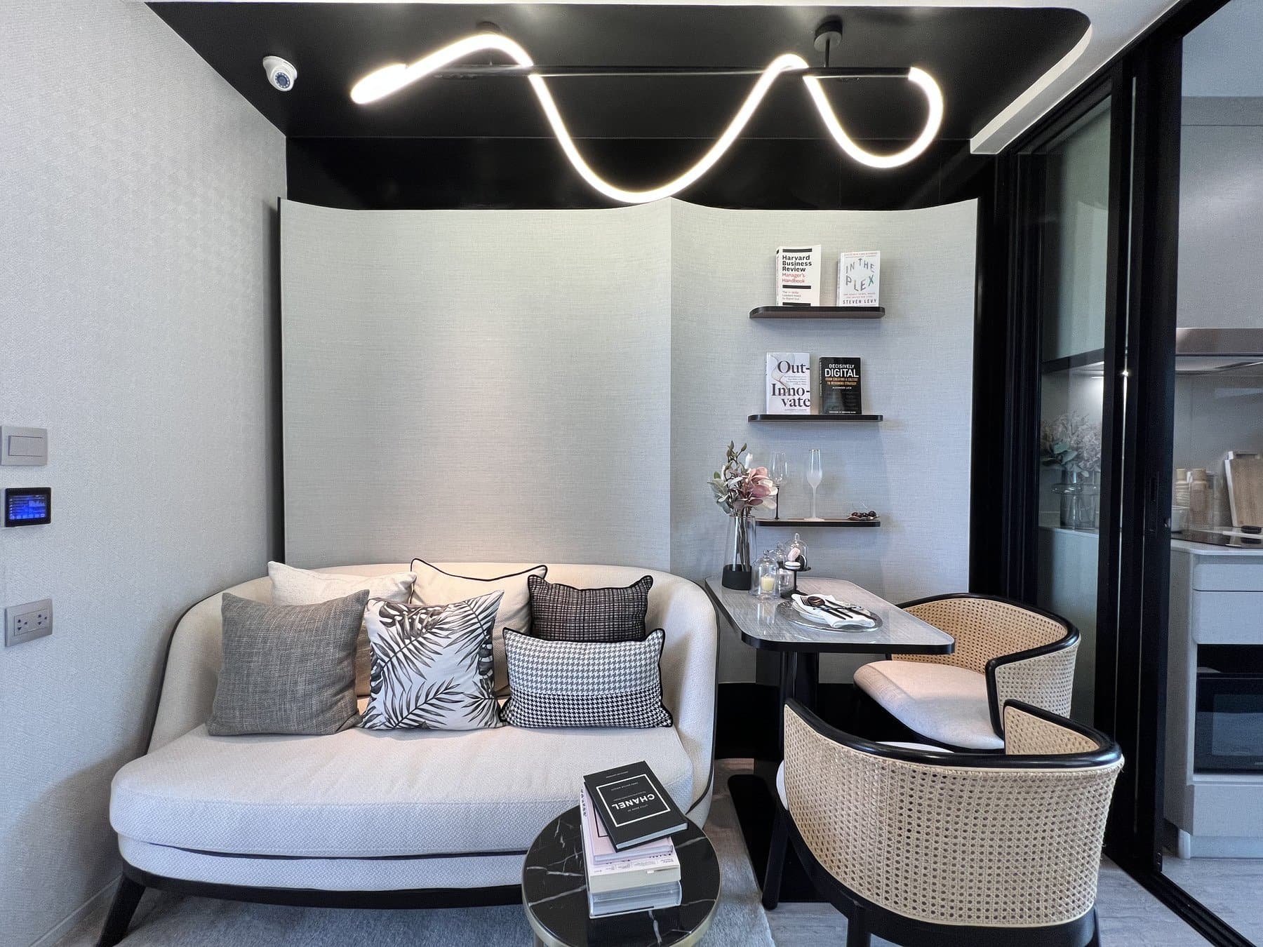 Seating and dining corner of a furnished show unit at Atmoz Oasis Onnut, with a rounded cream sofa, a bistro table and rattan chairs under a wave-shaped light