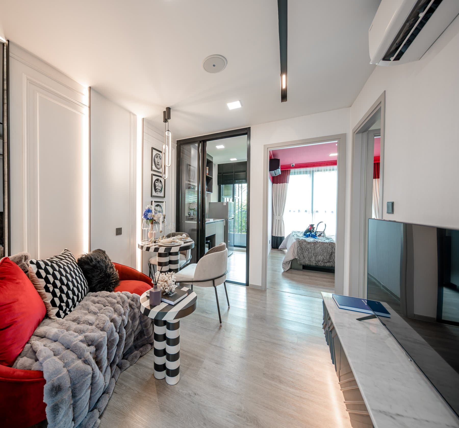 Living area of a furnished show unit at Atmoz Palacio Ladprao-Wanghin, with a red and grey sofa, a monochrome rug and a television facing the balcony door