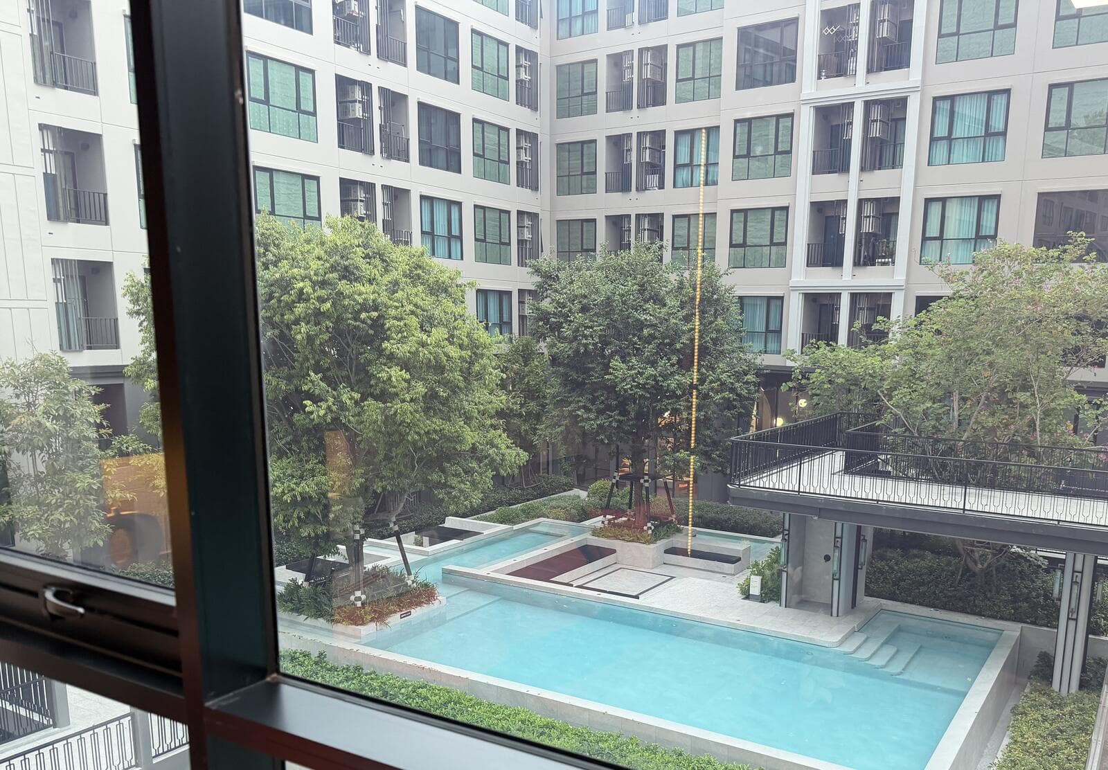Outlook from a show unit window over the Atmoz Palacio courtyard, showing the swimming pool, shaded deck and mature trees enclosed by the surrounding low-rise residential blocks.