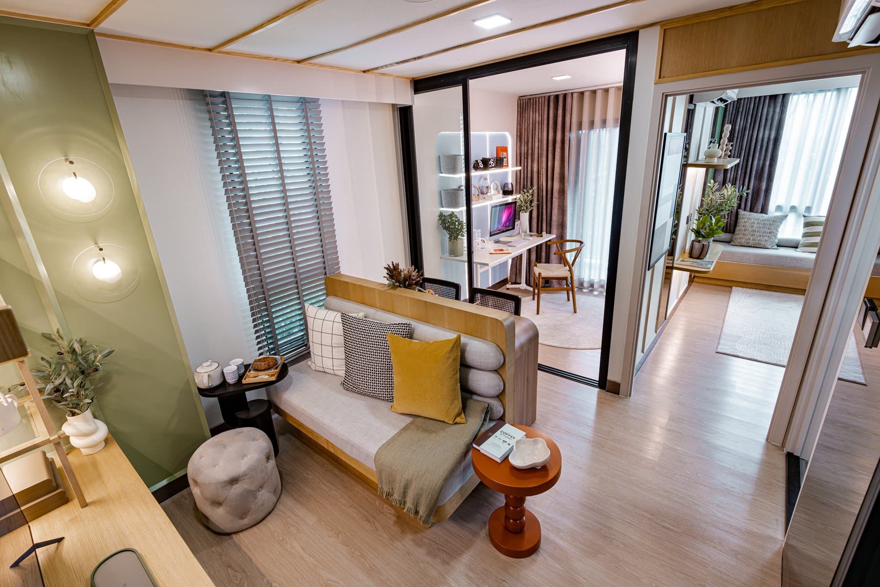Living area of a furnished show unit at Atmoz Season Ladkrabang, with a mustard cushioned bench, a round side table and louvred window blinds