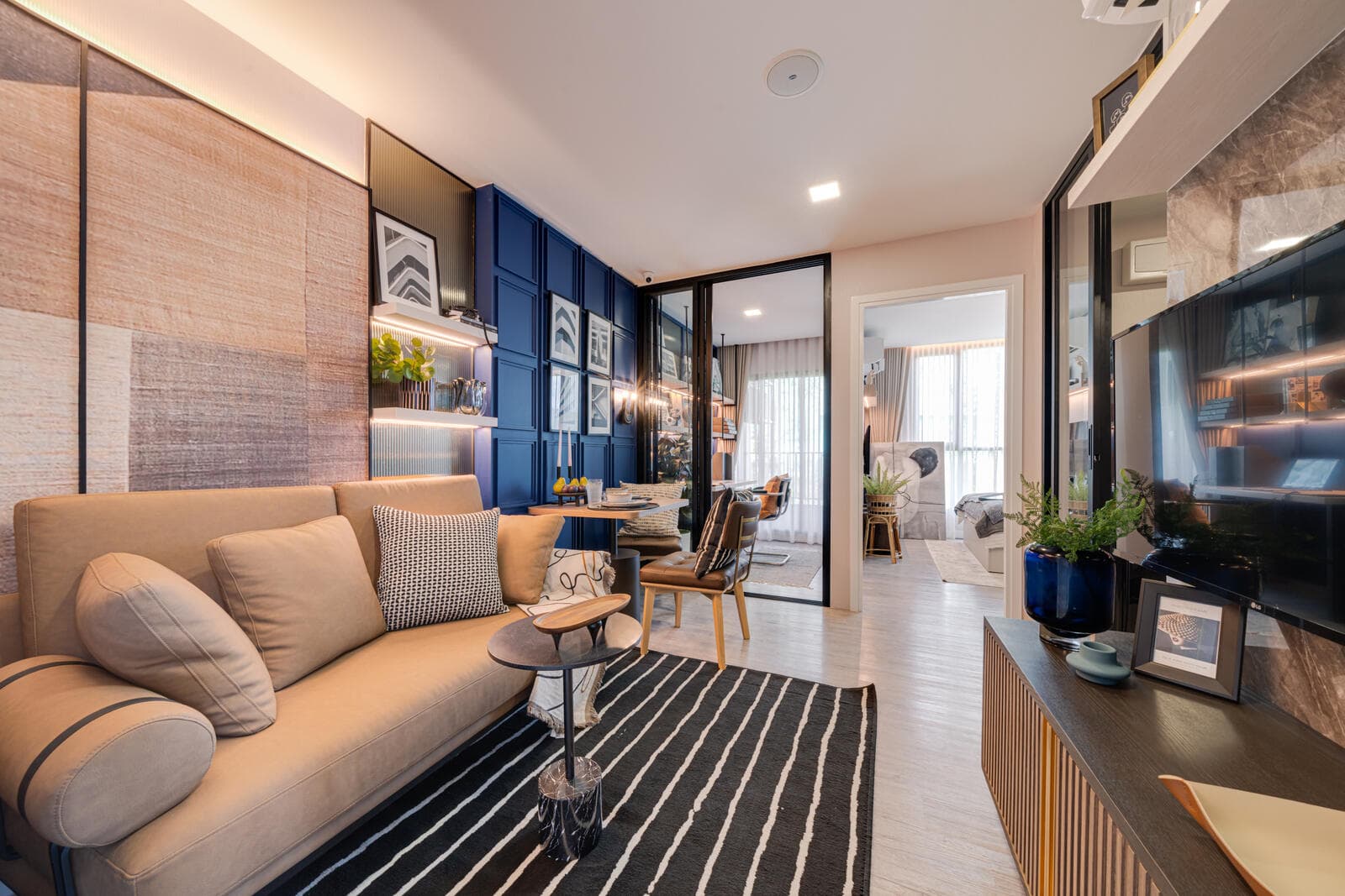 Show unit living area of a 1 Bedroom Plus layout with a fabric sofa, navy panelled wall and glass partition to the bedroom