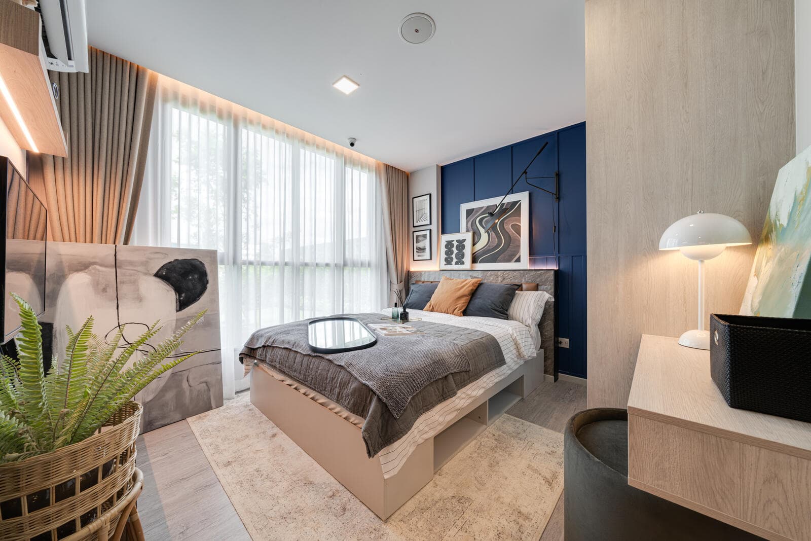 Show unit bedroom with a double bed against a navy panelled headboard wall and full-height sheer-curtained window