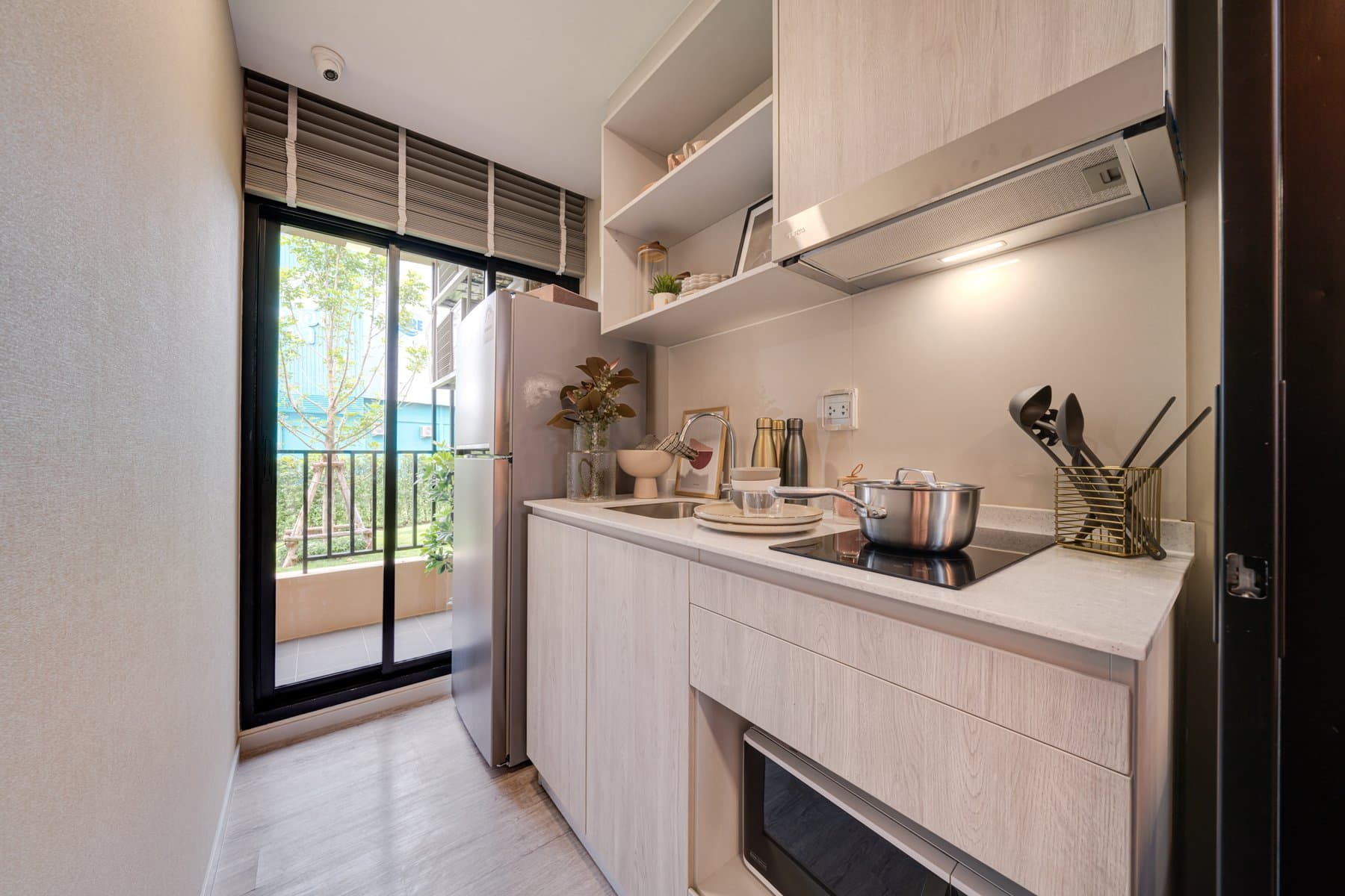 Kitchen of a furnished show unit at Atmoz Portrait Srisaman, with pale timber cabinetry, a built-in hob and a sliding door opening to the balcony