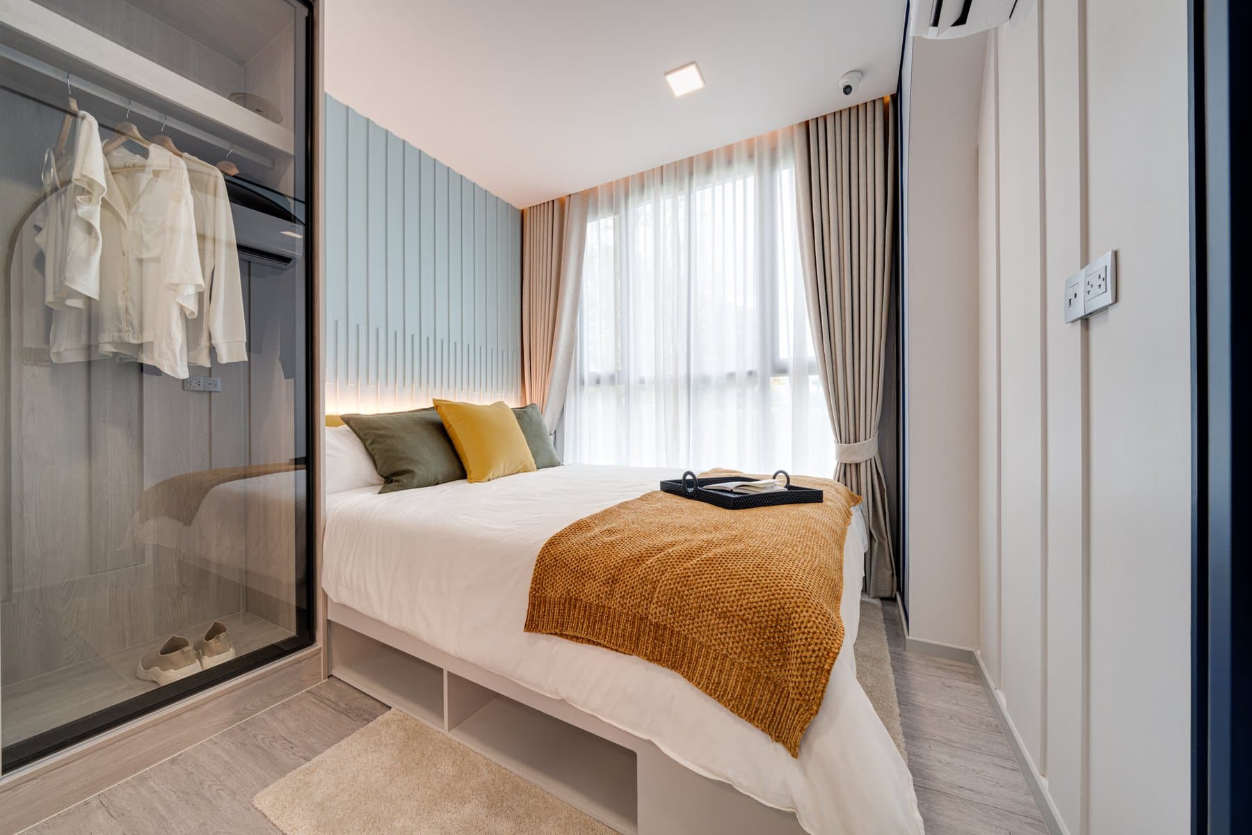 Bed and open wardrobe in a furnished show unit at Atmoz Portrait Srisaman, with hanging rails behind a glazed screen and a pale blue panelled wall