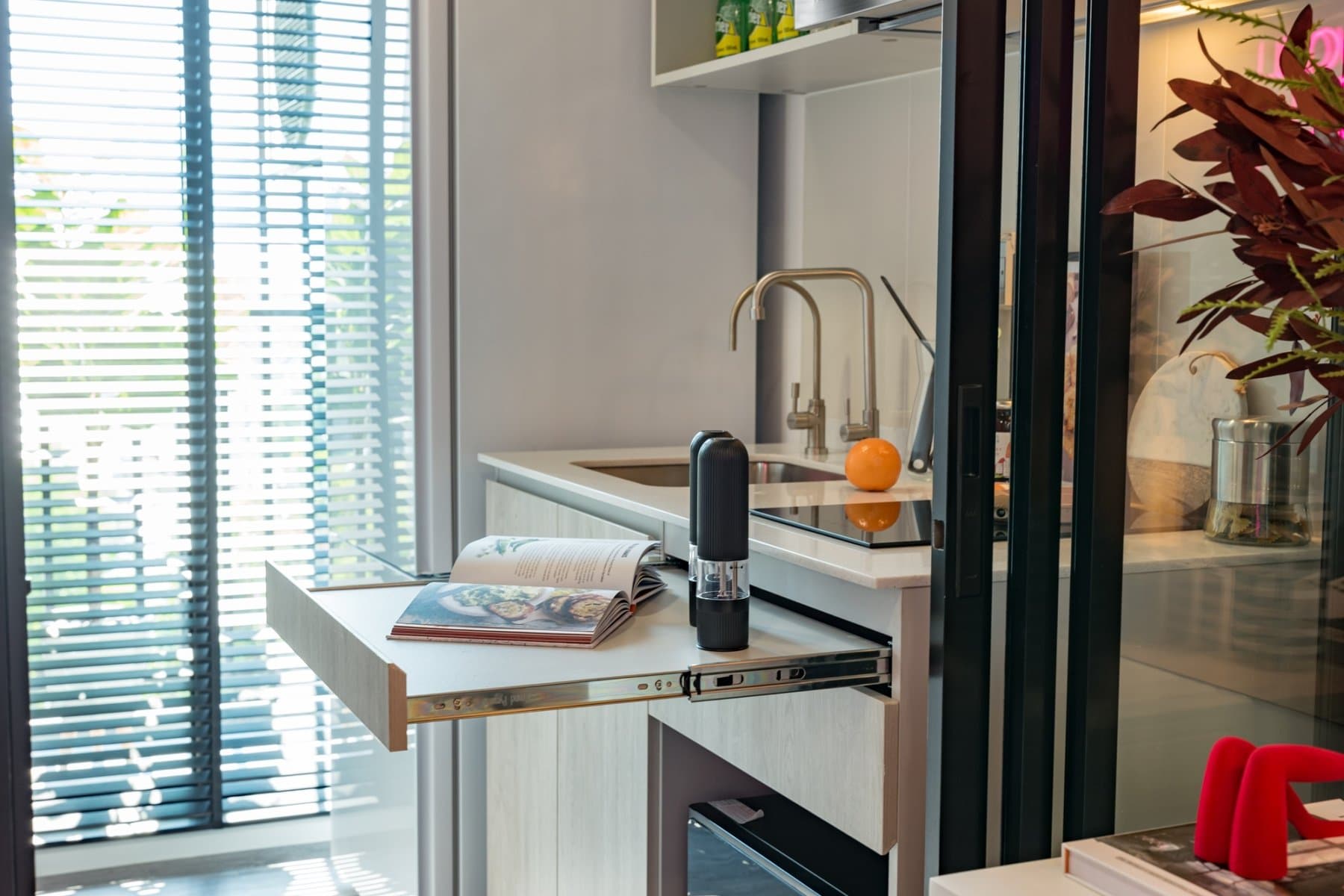 Kitchen of a furnished show unit at Atmoz Tropicana Bangna, with a brass tap, a coffee machine and a glazed screen through to the living area