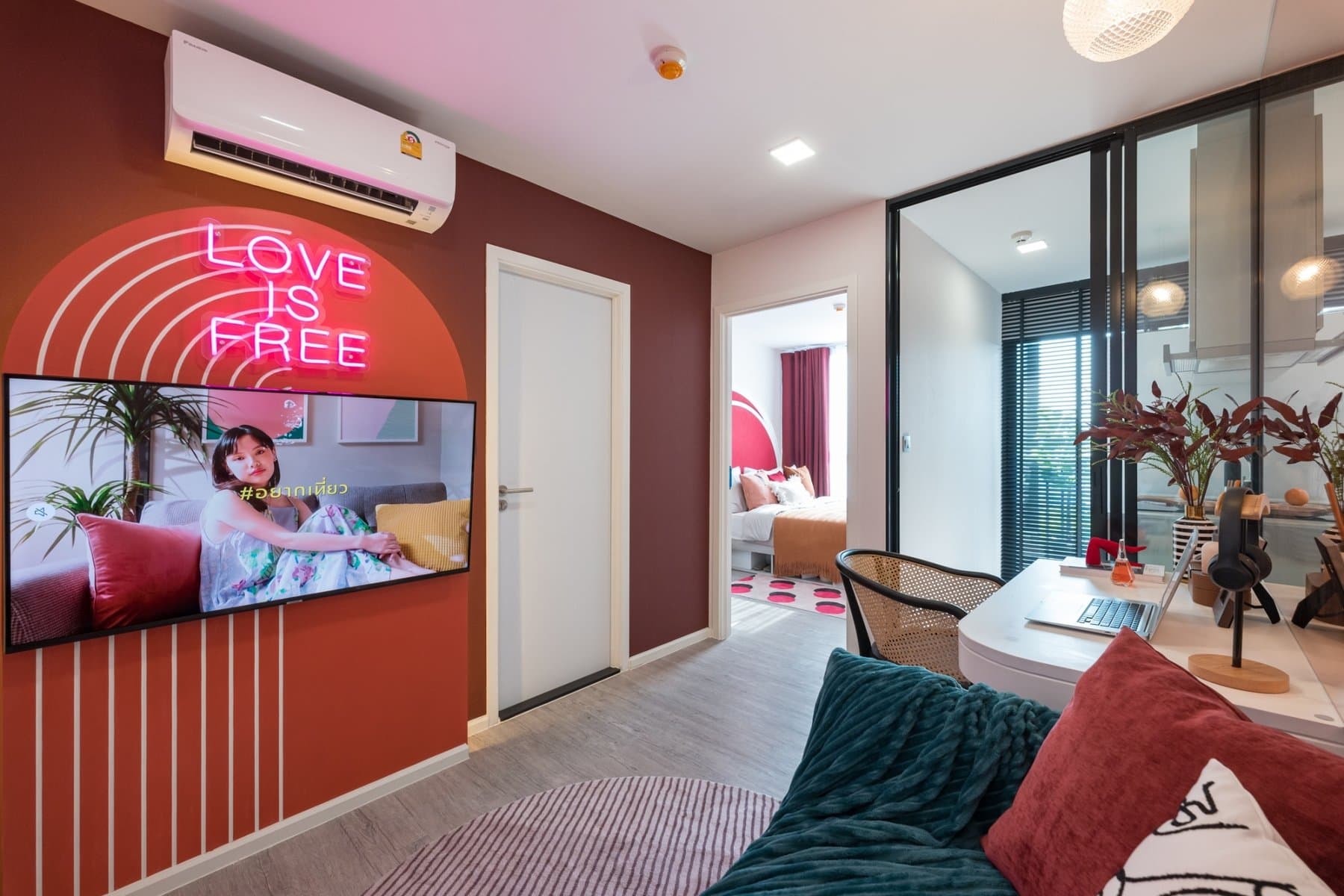 Living area of a furnished show unit at Atmoz Tropicana Bangna, with a coral fluted wall, a neon script sign and a wall-mounted television