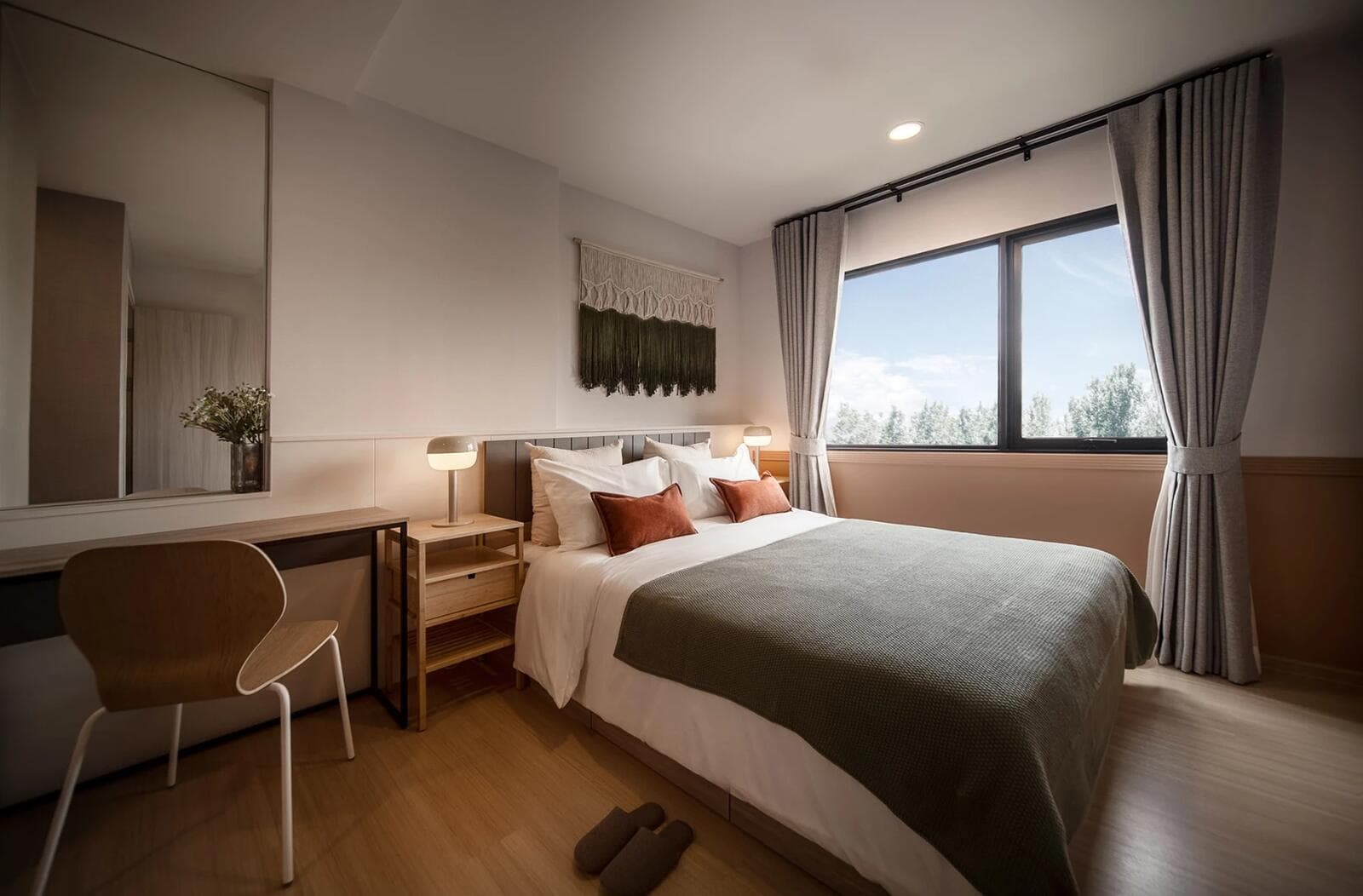 Photograph of a furnished show-unit bedroom with a double bed, bedside lamps, built-in desk and mirror, and a large window framed by full-length curtains.