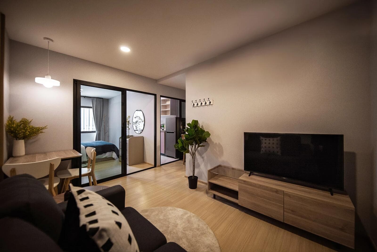 Photograph of a furnished show-unit living area with sofa, dining table, television console and sliding glass doors onto the bedroom and kitchen.