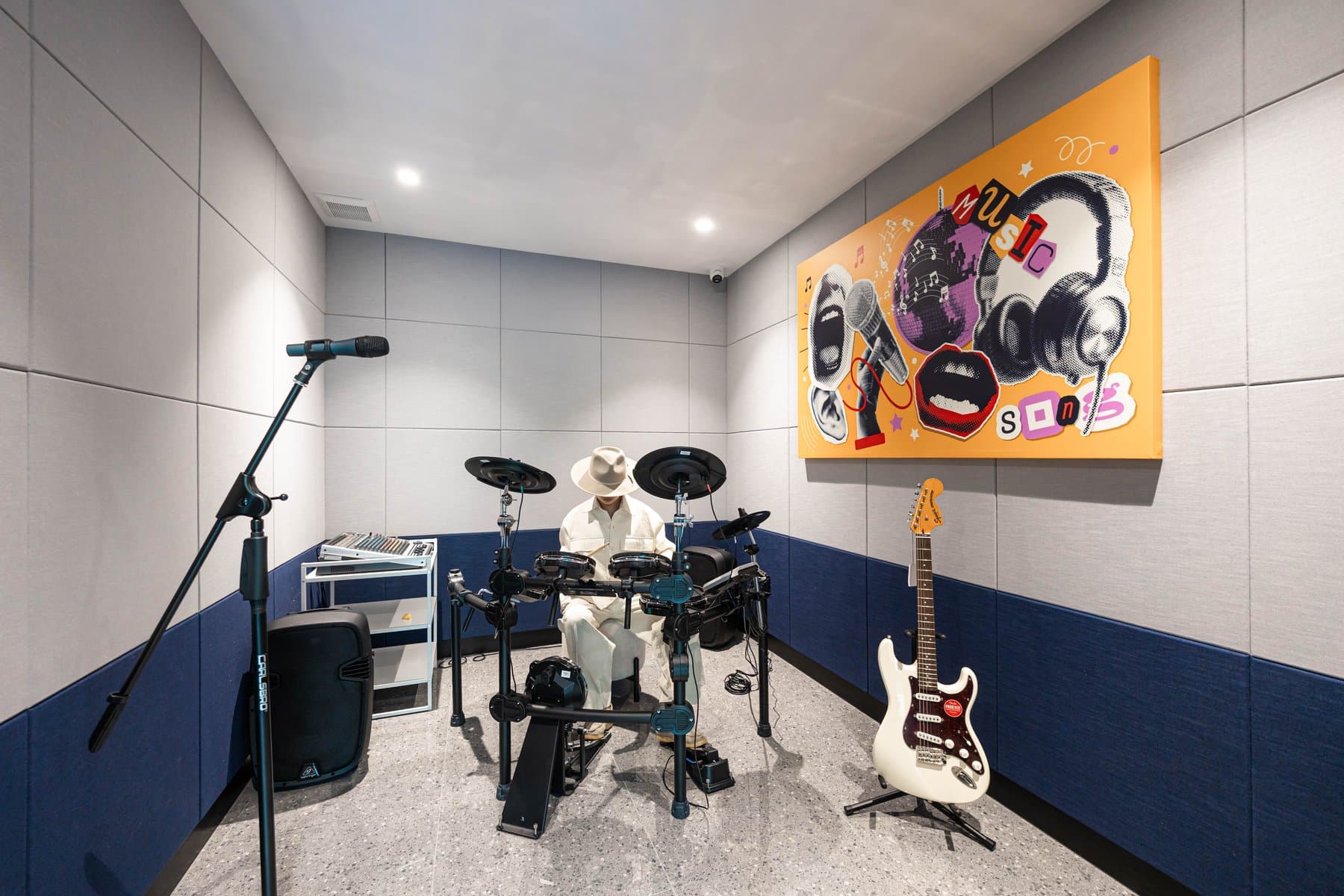 Music room at Kave COCO Bangsaen equipped with an electronic drum kit, an electric guitar and a microphone stand against a navy dado