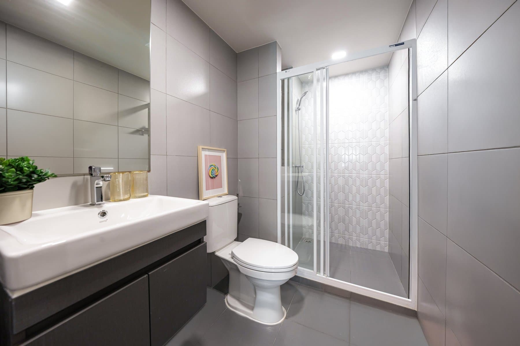Bathroom of a furnished unit at Kave COCO Bangsaen, with a wall-hung basin on a dark vanity, a mirror and a glazed shower enclosure