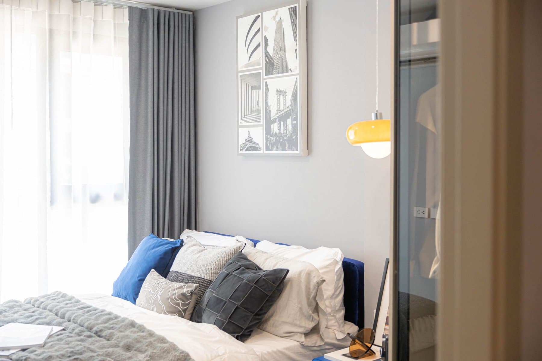 Bed and window of a furnished unit at Kave COCO Bangsaen, dressed in white and grey linen with a framed print above the headboard