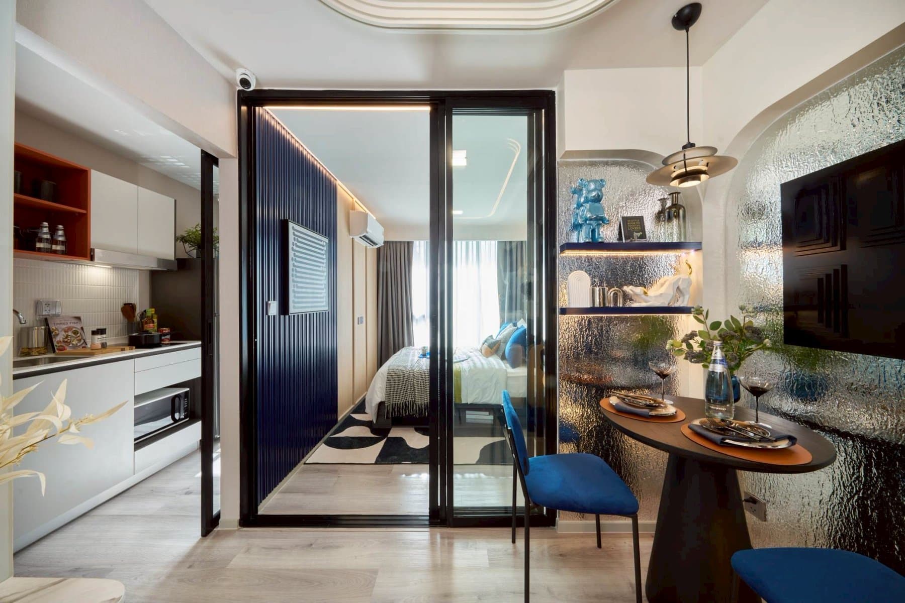 One Bedroom Exclusive at Kave Genesis showing the round dining table for two, the white kitchen run and the glazed sliding wall to the bedroom