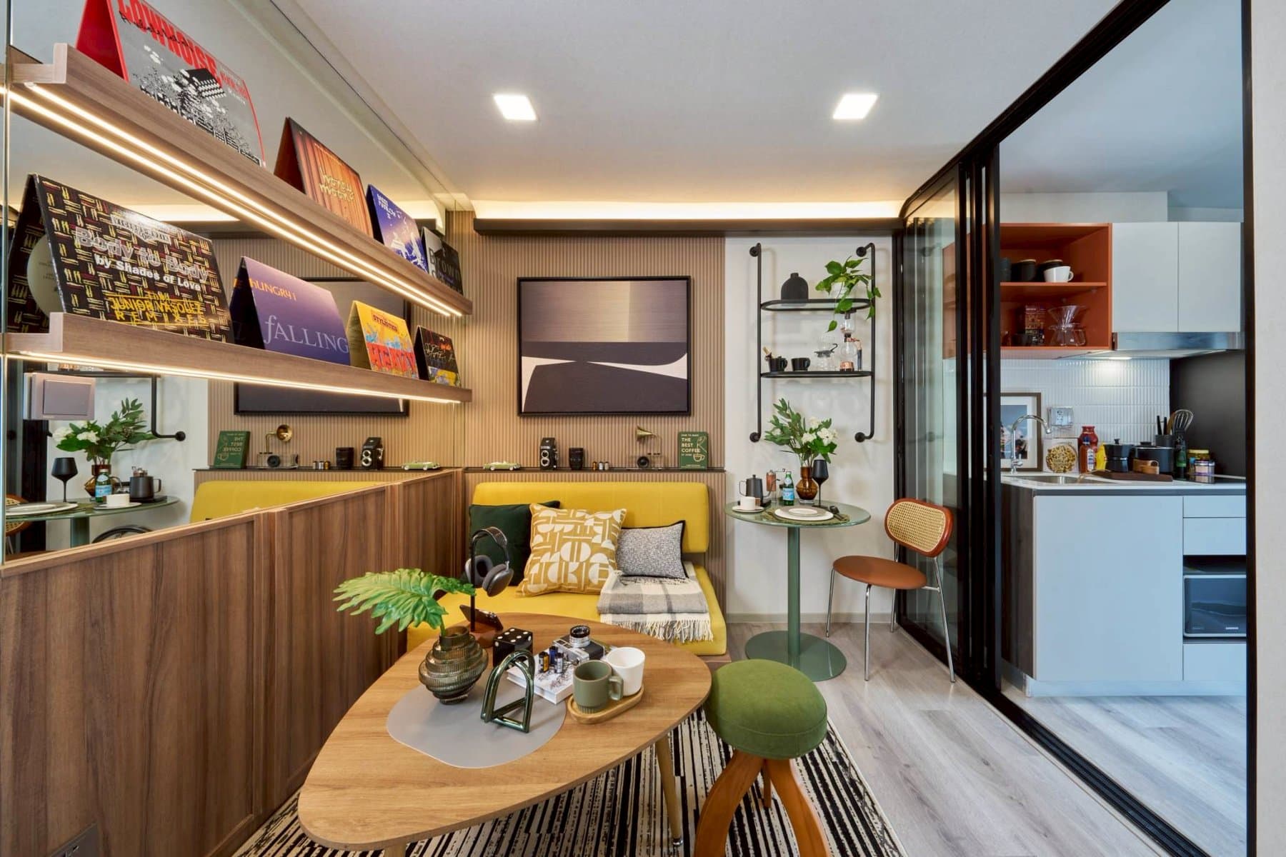 One Bedroom Extra show unit at Kave Genesis, with a mustard sofa, a round timber coffee table and a gallery shelf of framed prints above