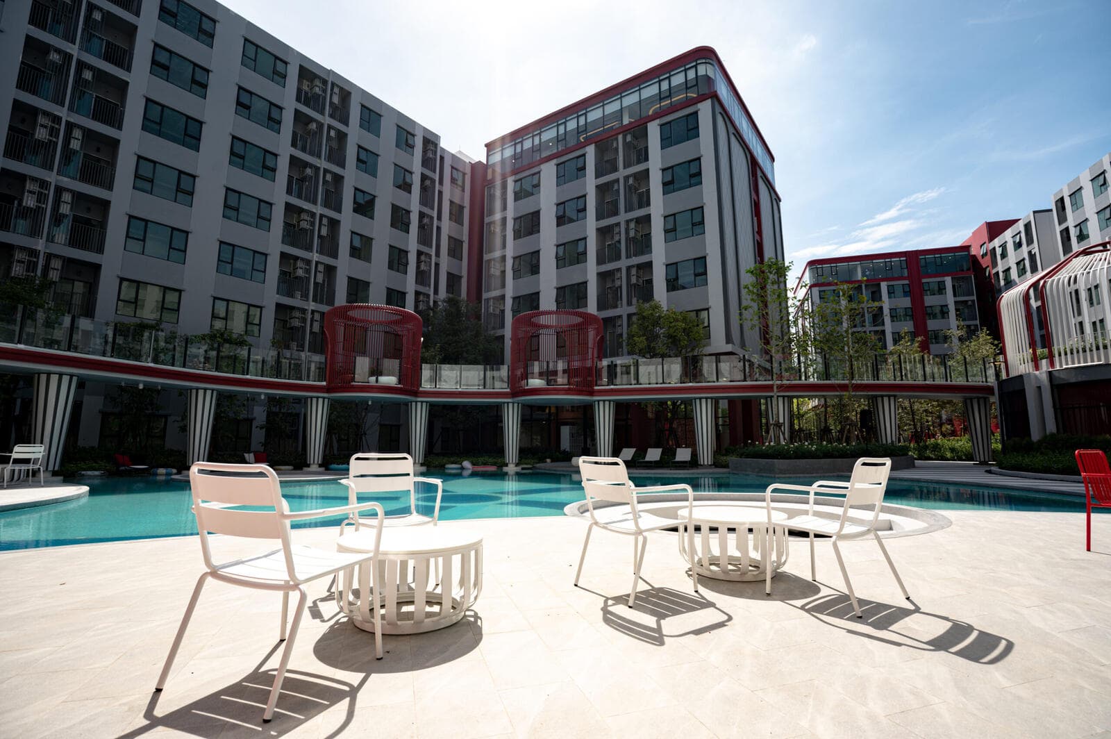Central courtyard swimming pool at Kave Wonderland with white poolside chairs and tables in front of the residential buildings