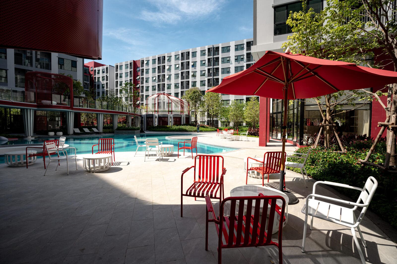 Poolside terrace at Kave Wonderland with red and white outdoor seating under a parasol beside the courtyard pool