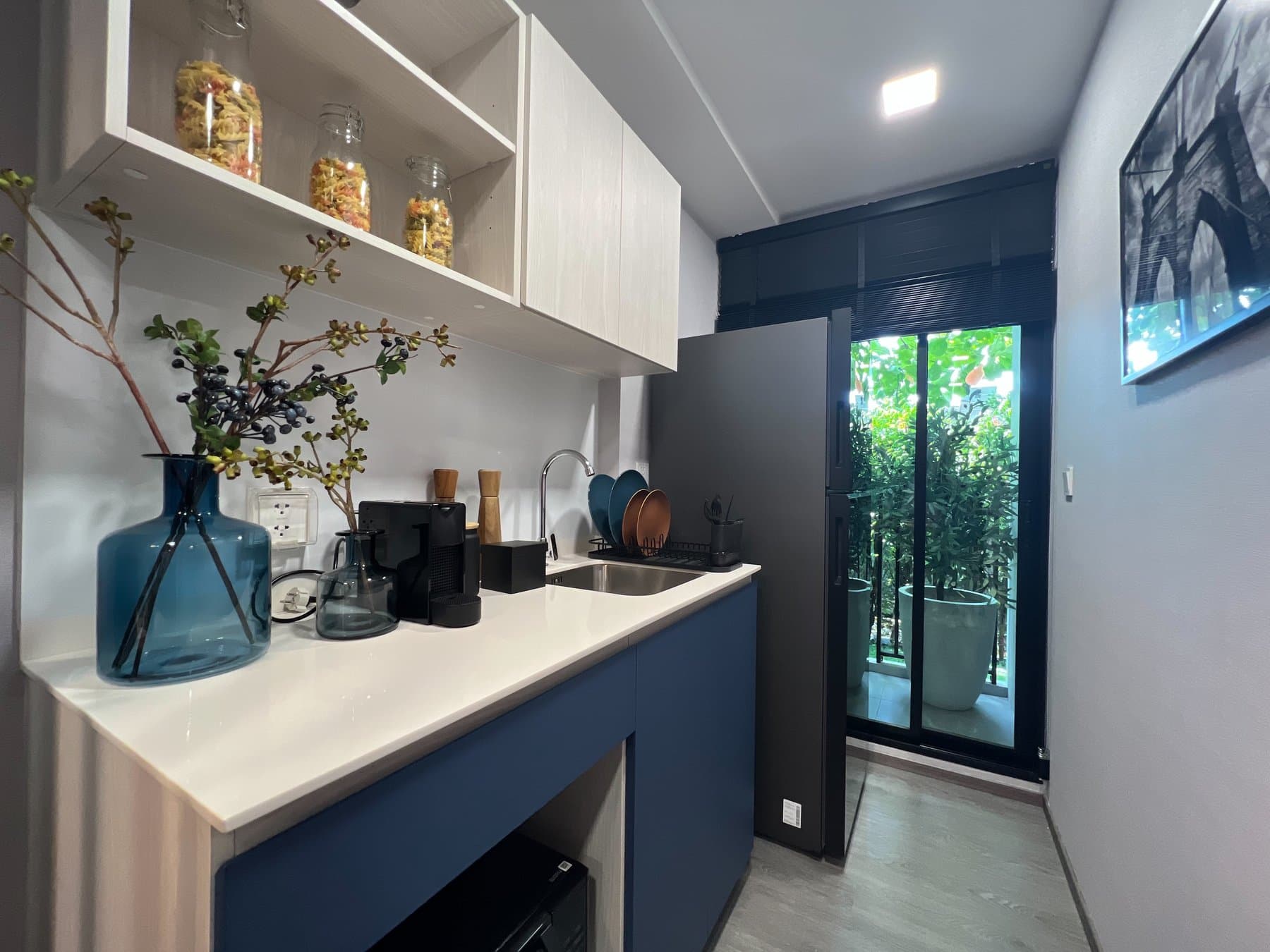 Kitchen run in a furnished show unit at Kave Wonderland, with navy base units, glass storage jars on the shelf and daylight from the balcony door