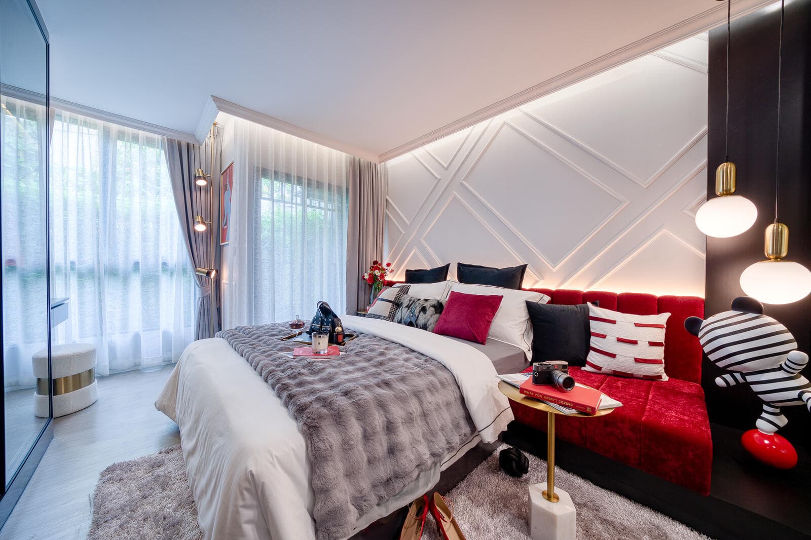 One-bedroom show unit bedroom with a fluted white feature wall, concealed cove lighting, red velvet window bench and full-height sheer-curtained windows.