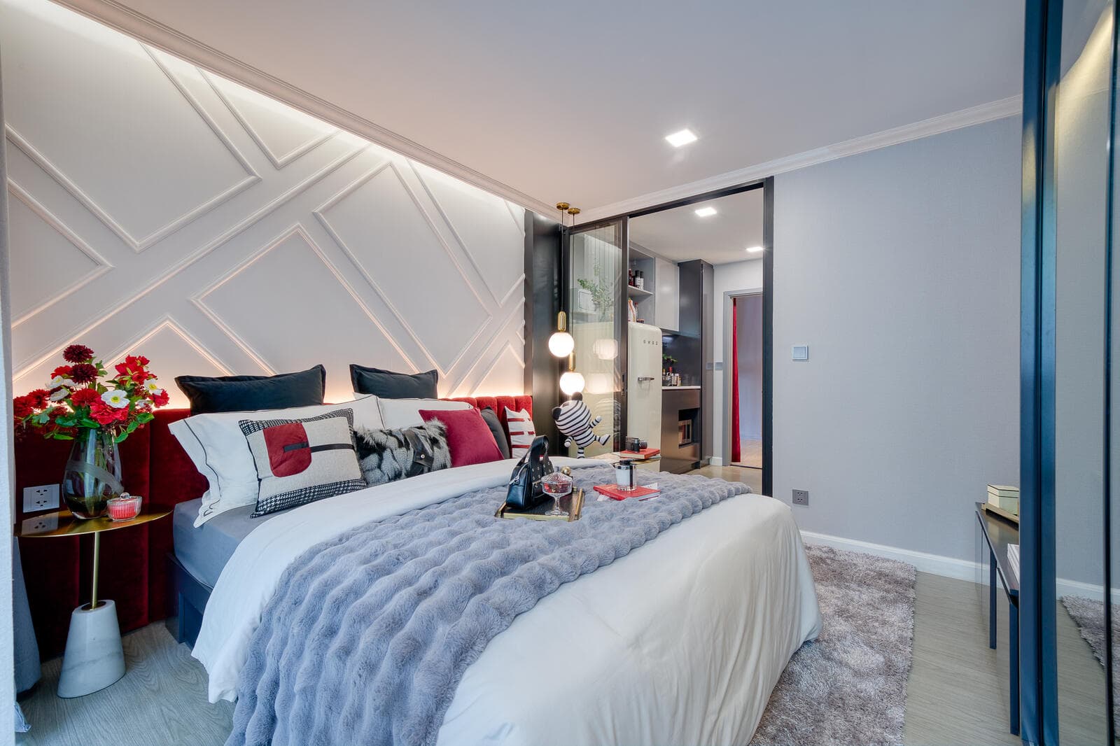 One-bedroom show unit bedroom looking toward the glazed sliding partition to the kitchenette, with panelled headboard wall and light timber flooring.