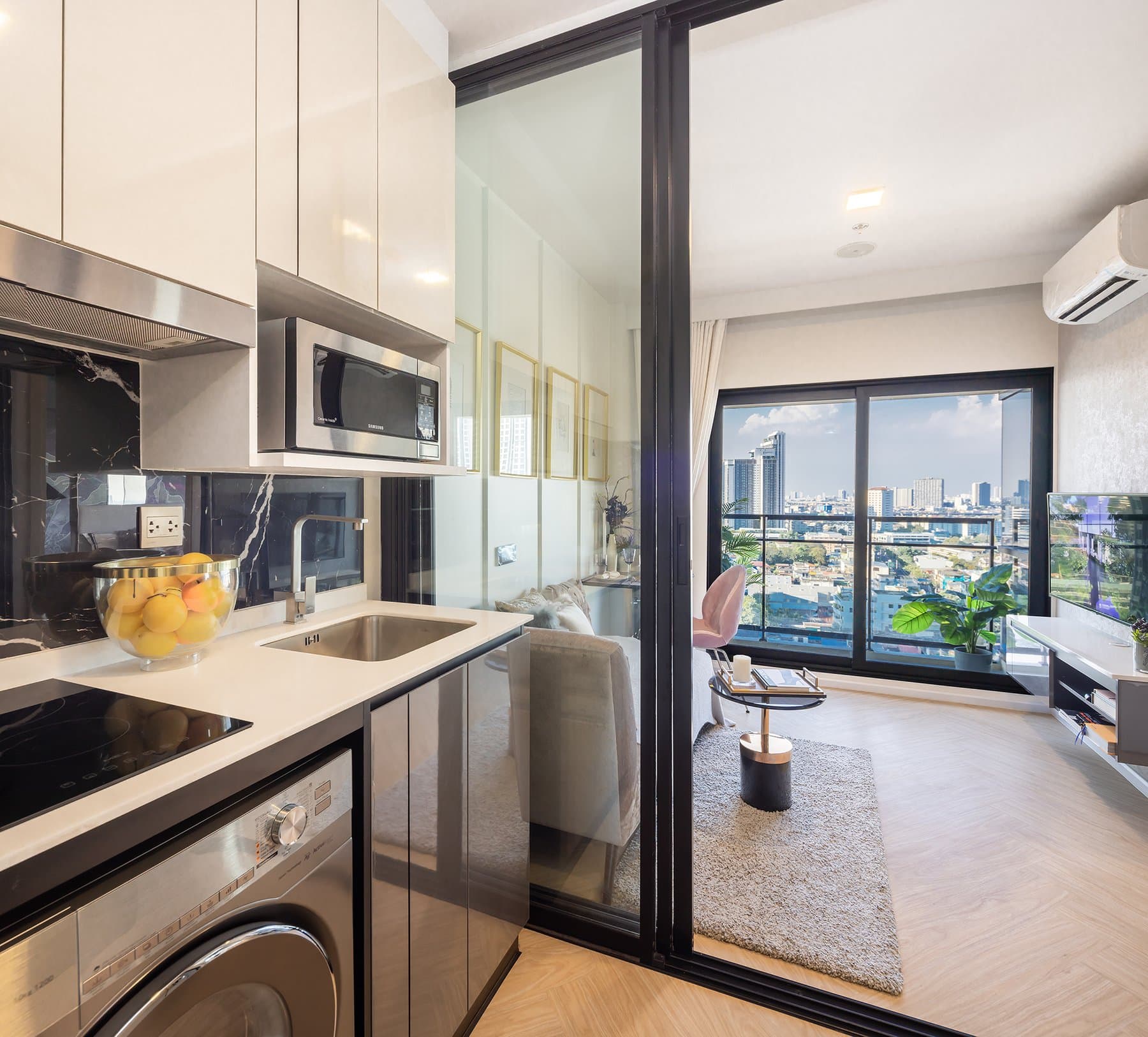 Kitchen of a furnished show unit at Modiz Collection Bangpho, with a washing machine below the counter and a glazed screen opening onto a high-level river outlook