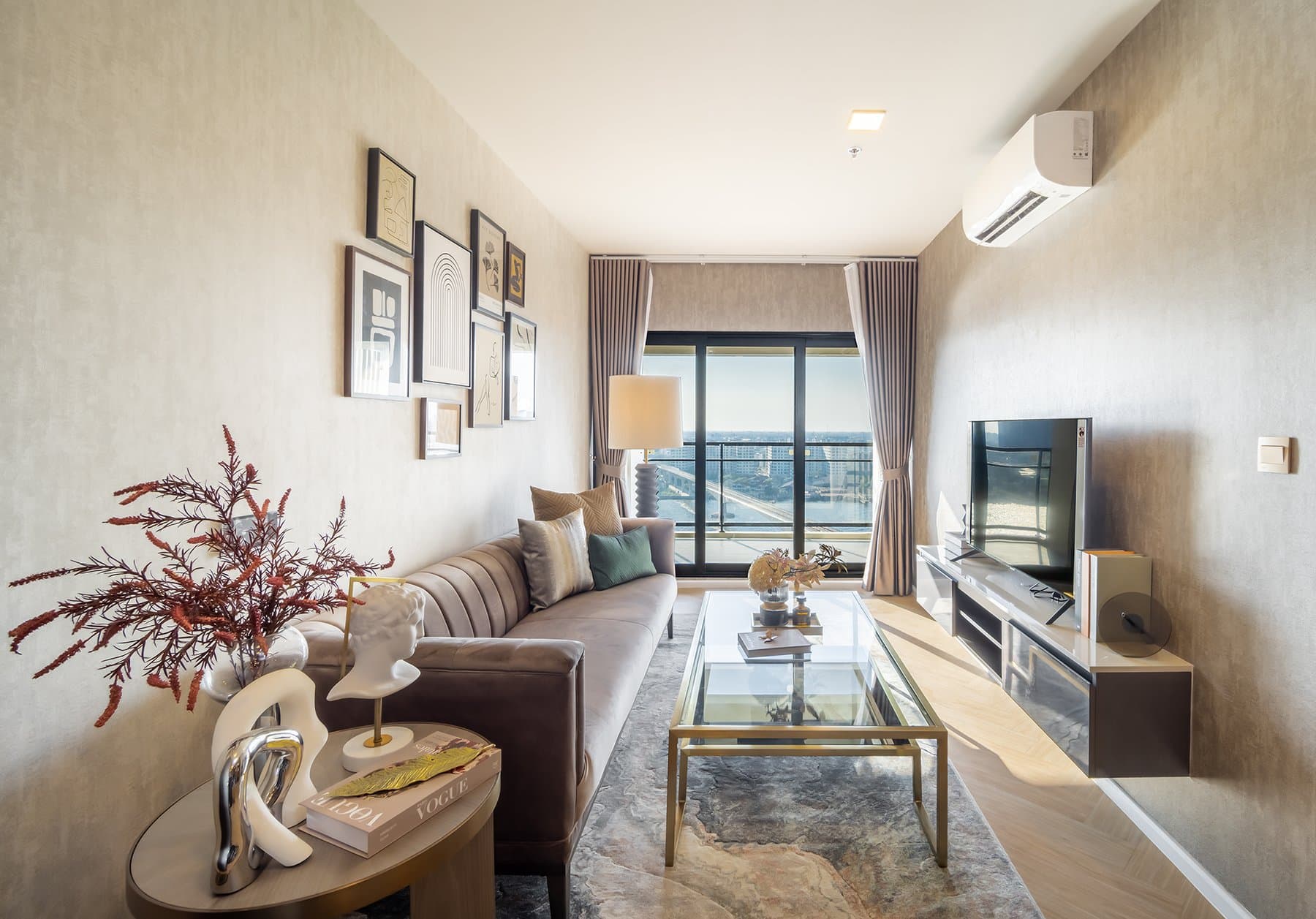 Living area of a furnished show unit at Modiz Collection Bangpho, with a pale sofa, a glass coffee table and full-height glazing onto the skyline