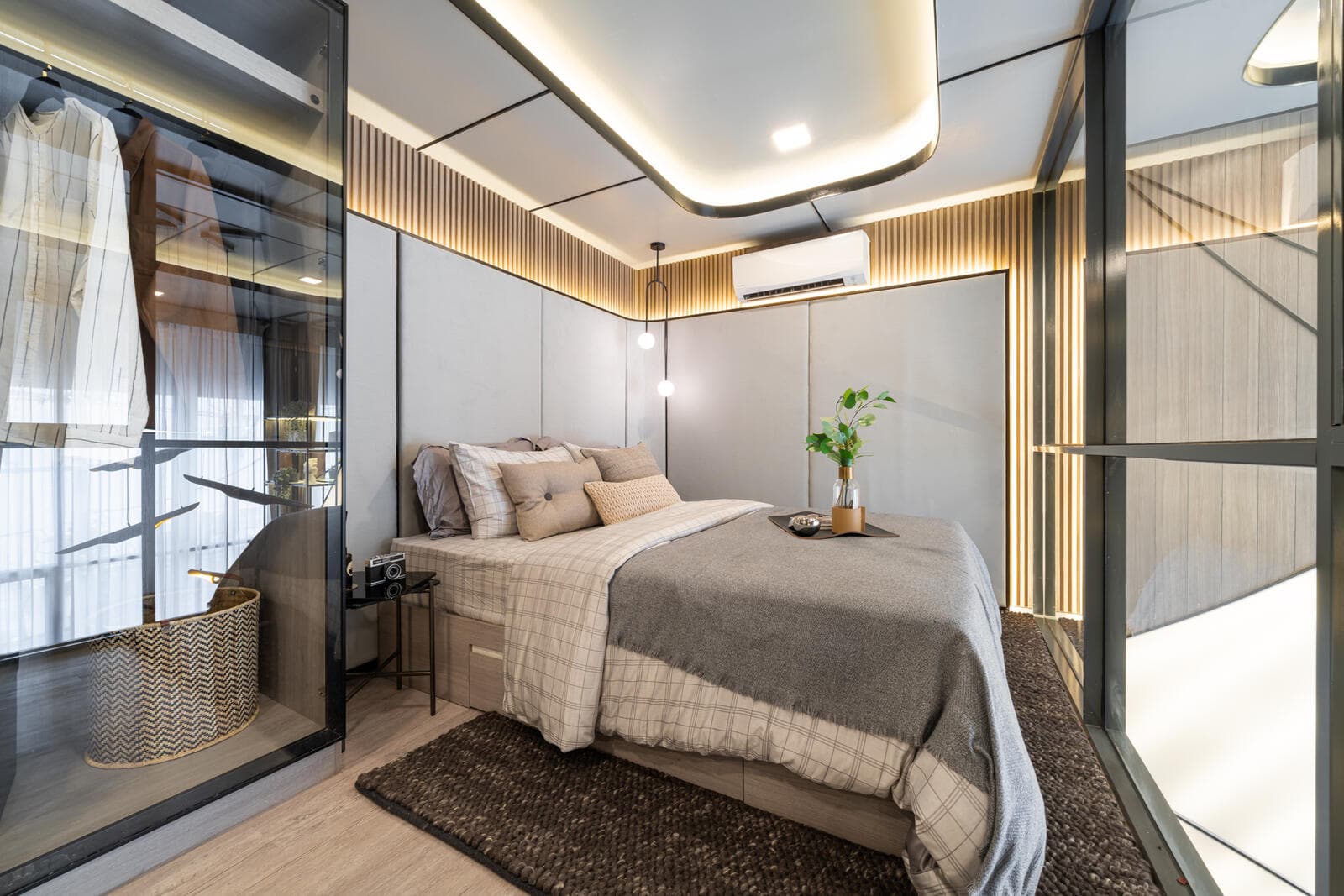 Show unit bedroom at Modiz Rhyme Ramkhamhaeng with an upholstered headboard wall, backlit slatted ceiling detail, glass-fronted walk-in wardrobe and a woven rug