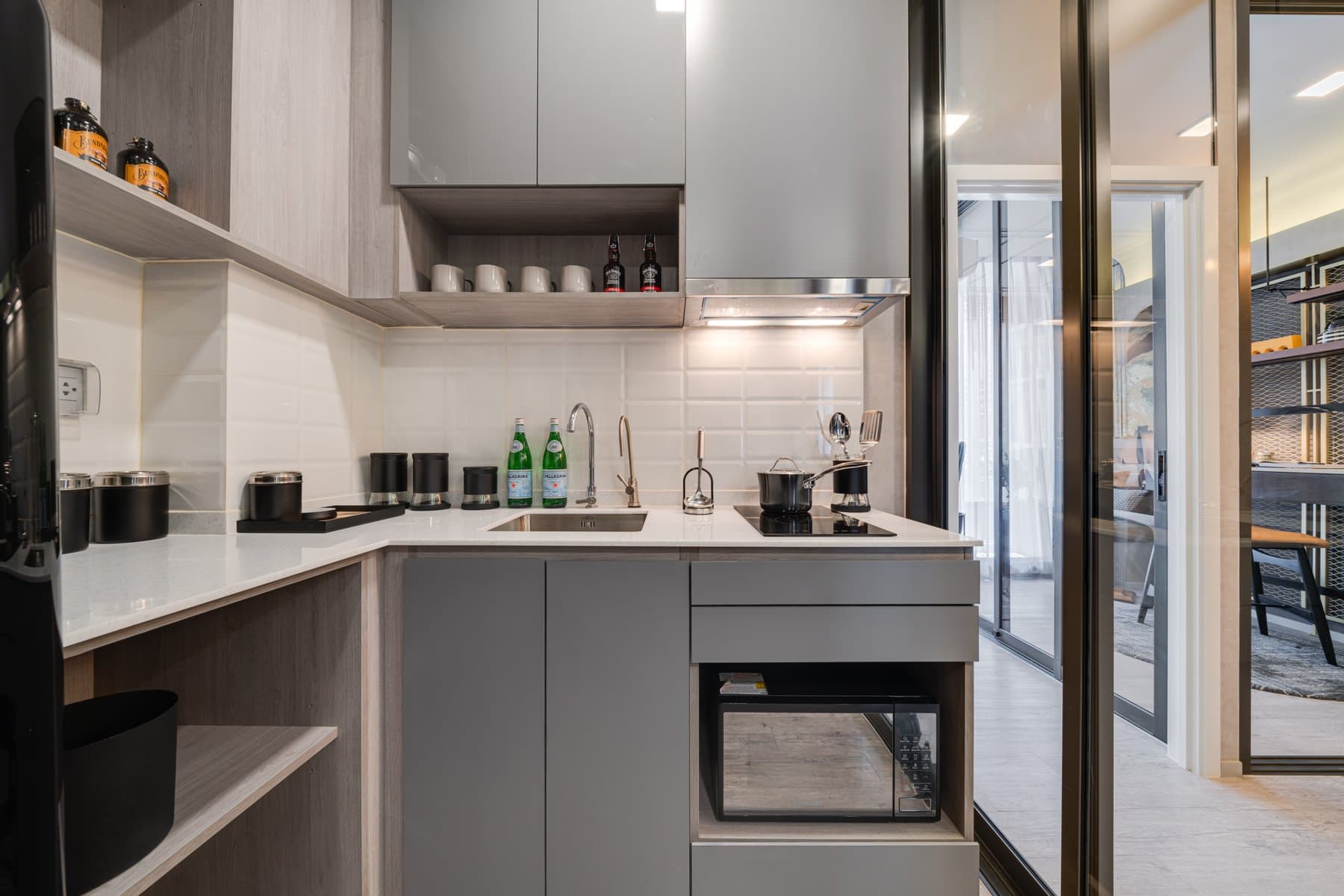 Kitchen of a furnished show unit at Modiz Rhyme Ramkhamhaeng, with a corner counter, a built-in oven and open shelving beside the balcony door