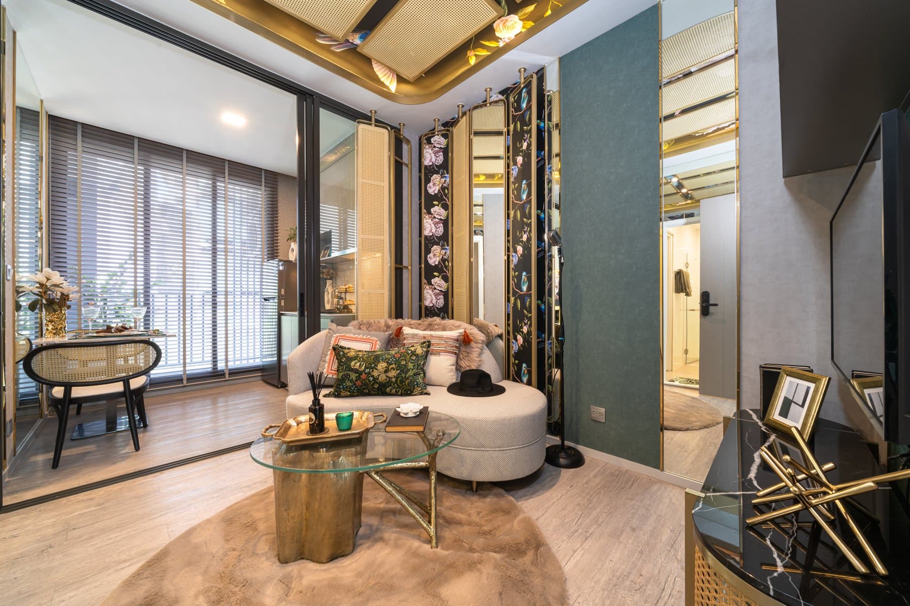 Living area of a furnished show unit at Modiz Rhyme Ramkhamhaeng, with a curved cream sofa, brass side tables and mirrored joinery