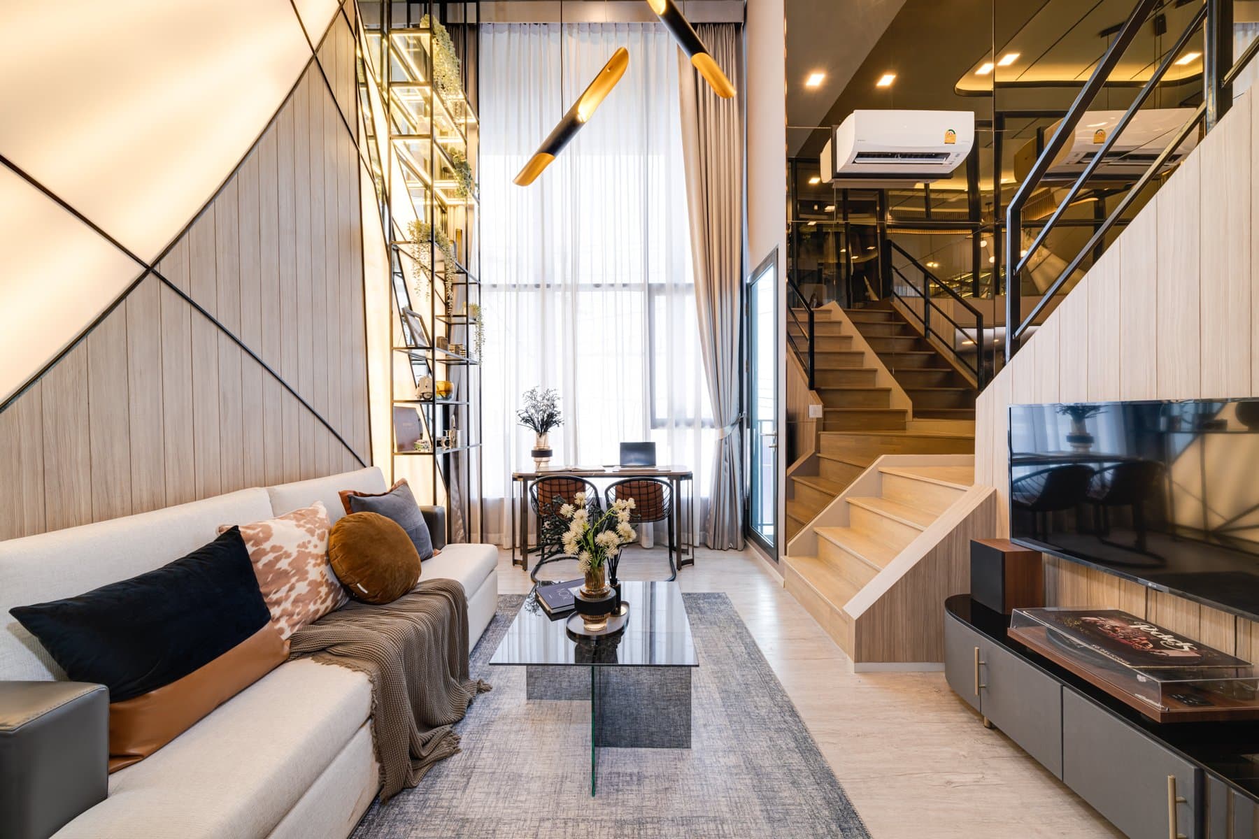 Living area of a vertical-suite show unit at Modiz Rhyme Ramkhamhaeng, with a pale sofa, timber panelling and the mezzanine stair behind