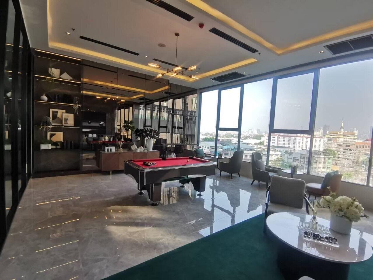Residents' games lounge at Modiz Sukhumvit 50 with a red-baize pool table, polished stone floor, pendant lighting and floor-to-ceiling windows overlooking the surrounding neighbourhood