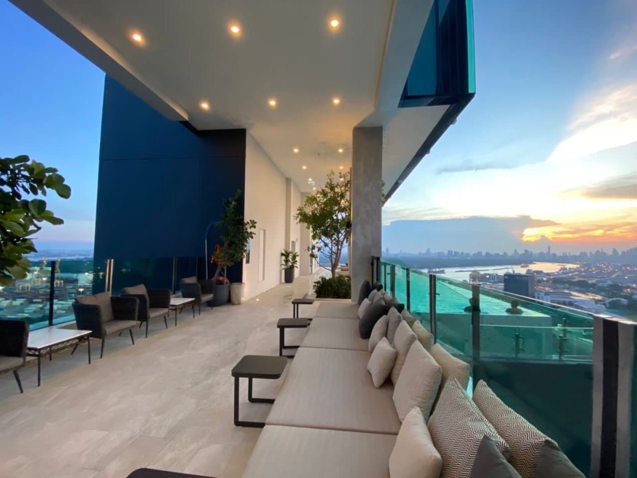 Sky lounge at Modiz Sukhumvit 50 at sunset, with a run of cushioned bench seating along the glazing and the city skyline beyond