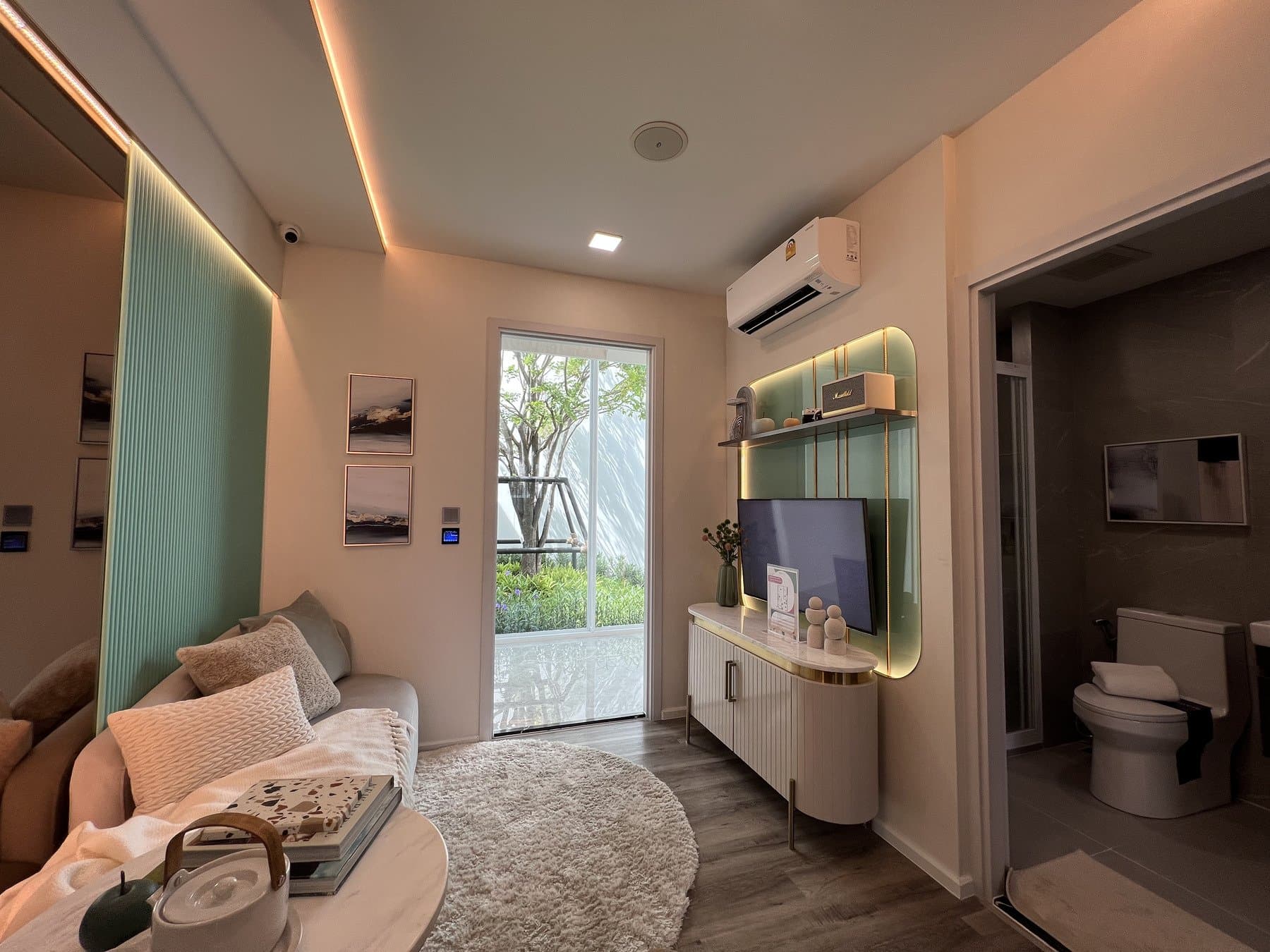 Living area of a furnished show unit at Modiz Vault, with a pale sofa, a green accent panel and the bathroom door open at the far end