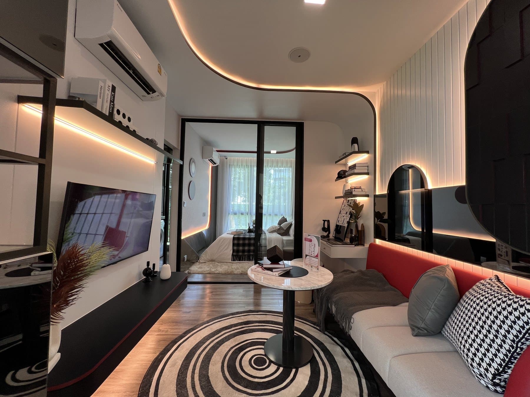 Living area of a second furnished show unit at Modiz Vault, with a red-cushioned sofa, a spiral-patterned rug and an arched cove light