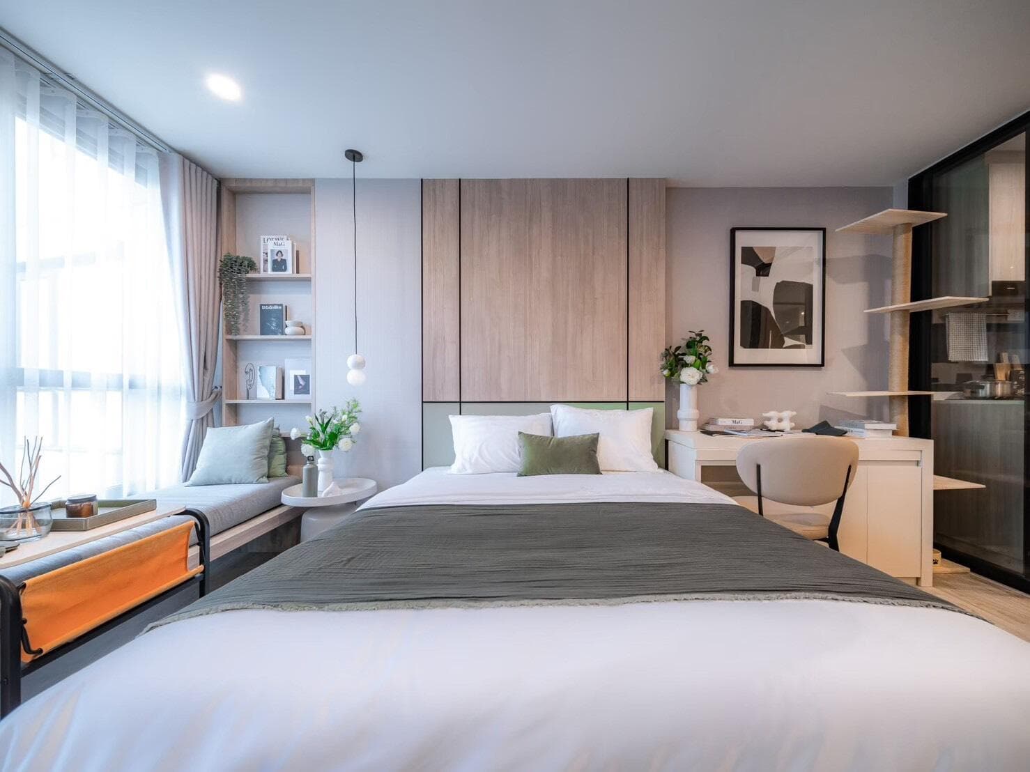 Show unit photograph of a studio bedroom at Origin Play Sri Udom Station with a built-in headboard wall, window bench seat, study desk and open shelving.
