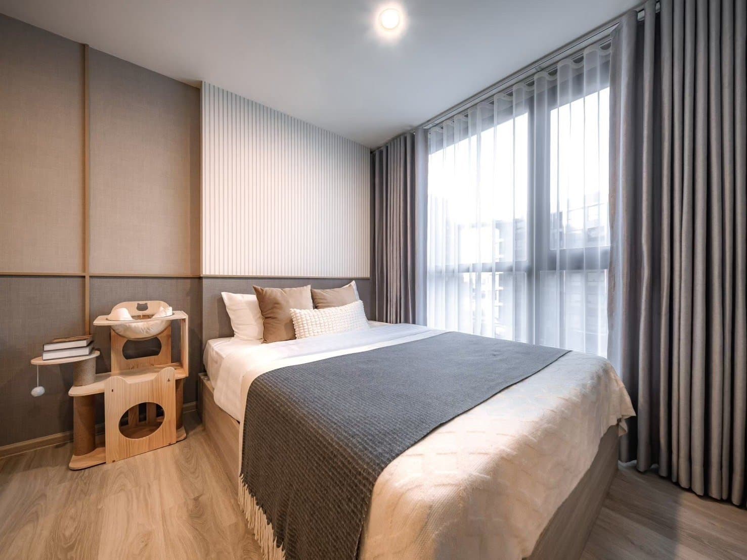 Bedroom of a furnished show unit at Origin Play Sri Udom Station, dressed in grey and white linen with a timber cat tower beside the curtained window