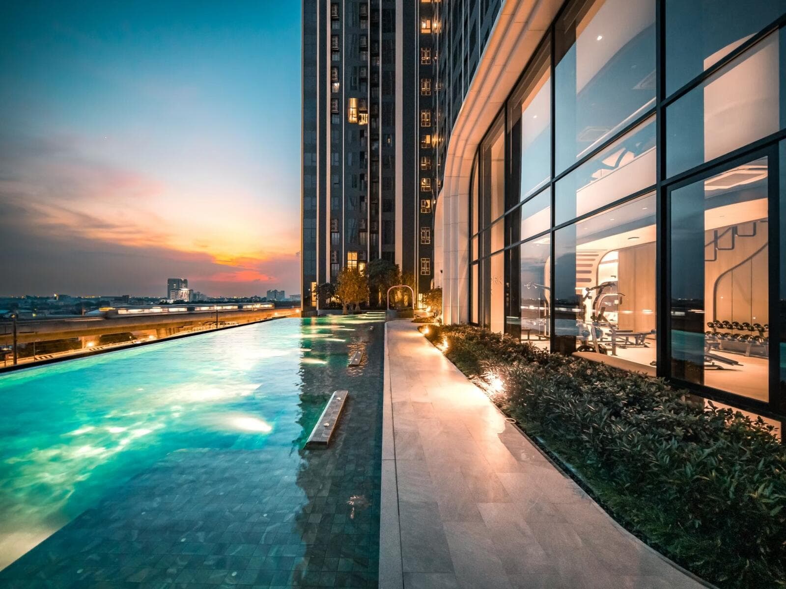 Photograph of the lit swimming pool at dusk alongside the glazed fitness room at Origin Plug & Play Nonthaburi Station.