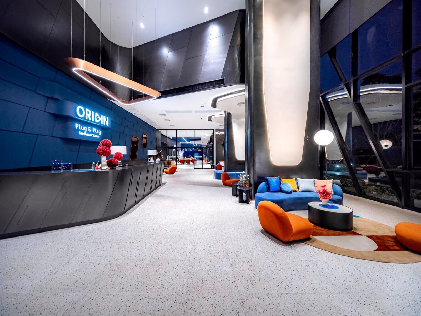 Photograph of the ground-floor lobby and reception counter at Origin Plug & Play Nonthaburi Station, with terrazzo flooring and lounge seating.