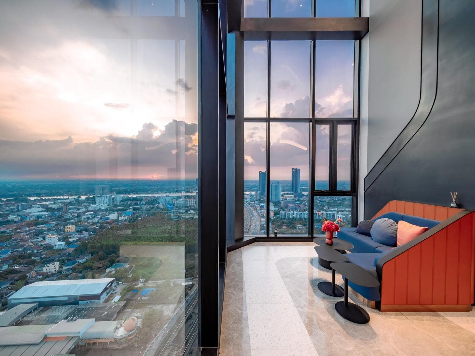 Photograph of the double-height sky lounge window at sunset, looking out over Nonthaburi, the Chao Phraya river and the expressway.