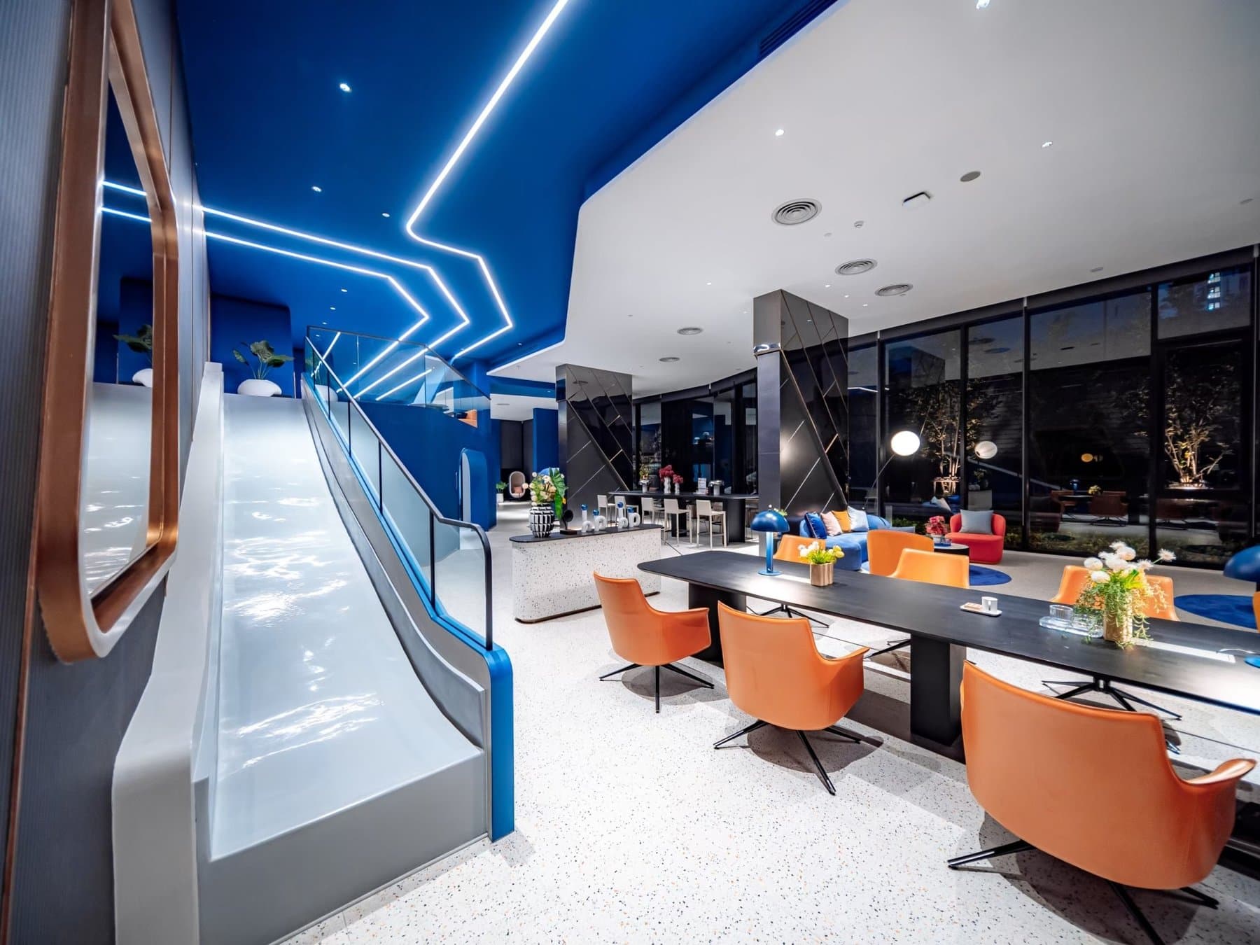 Co-working room at Origin Plug & Play Nonthaburi Station, with long shared tables, tan chairs and a curved white tunnel feature lit in blue