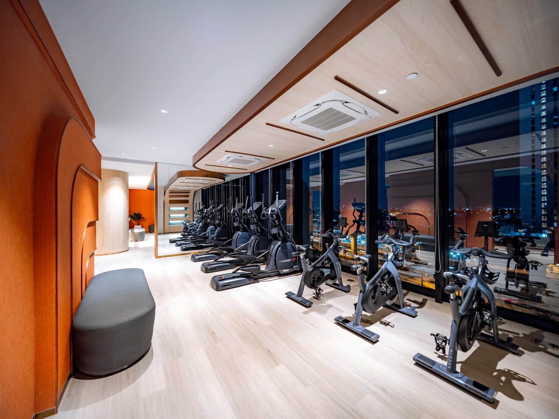 Fitness room at Origin Plug & Play Nonthaburi Station, with rows of exercise bikes along the window wall and an orange curved ceiling detail