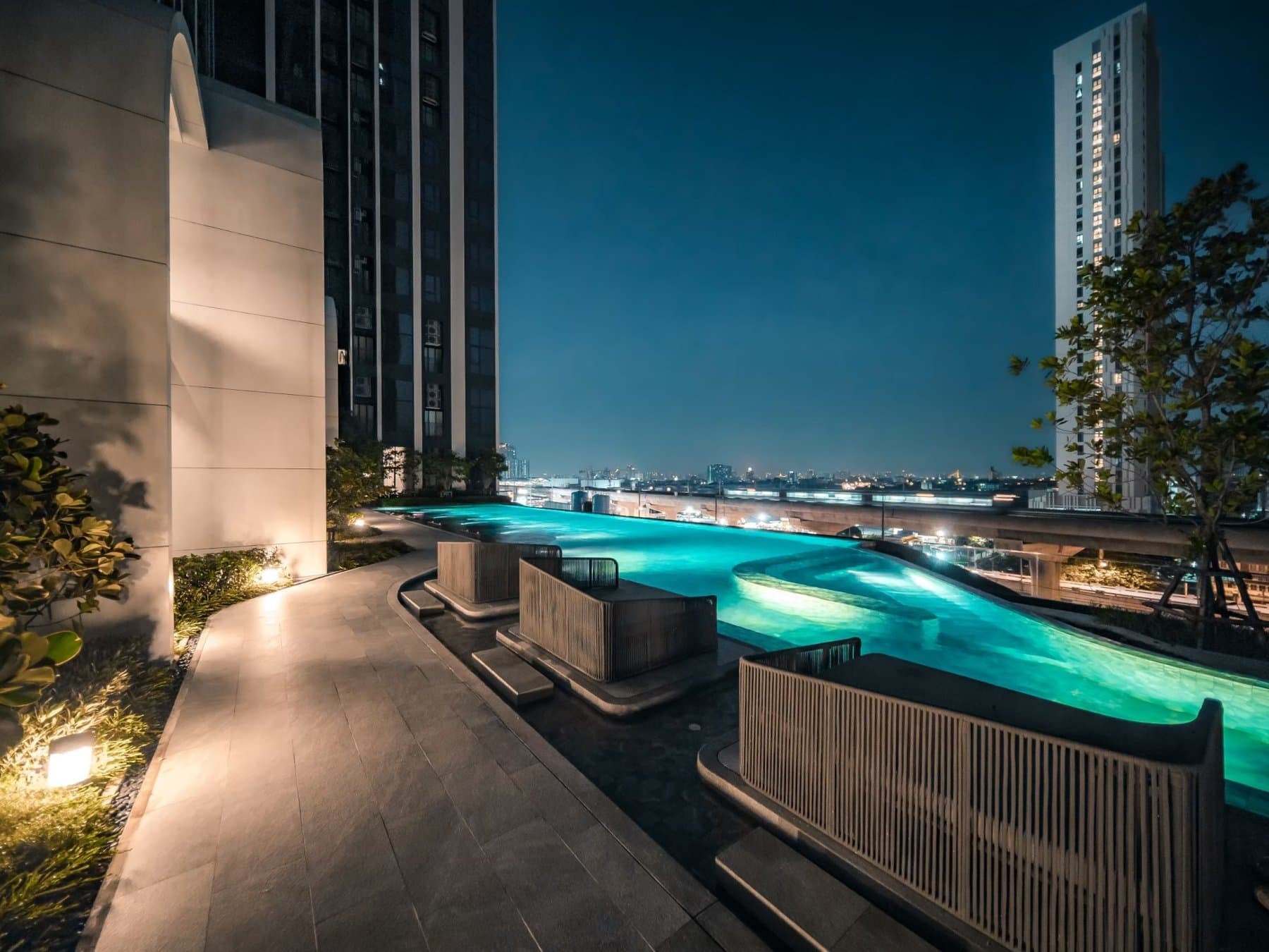 Rooftop pool at Origin Plug & Play Nonthaburi Station lit at dusk, with the water glowing against the darkening skyline
